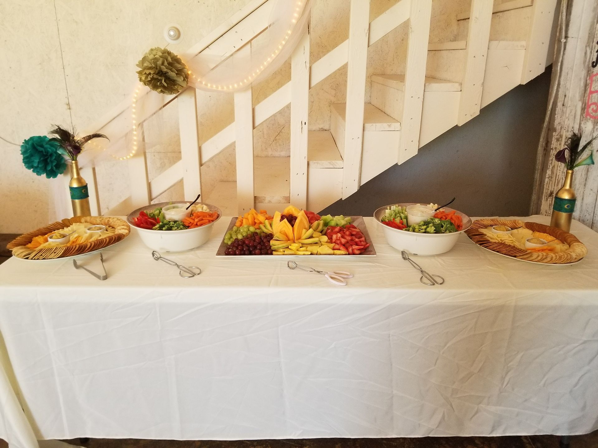 Buffet table with assorted dishes and fruit under a staircase at an indoor event
