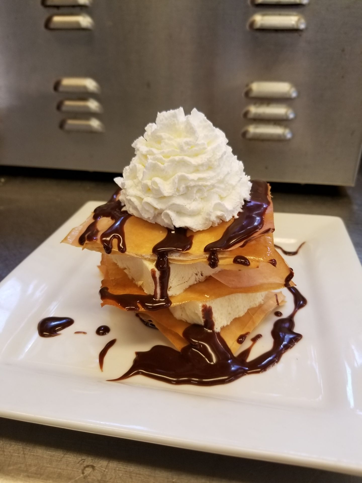 Stack of pancakes topped with whipped cream and chocolate drizzle on a white plate