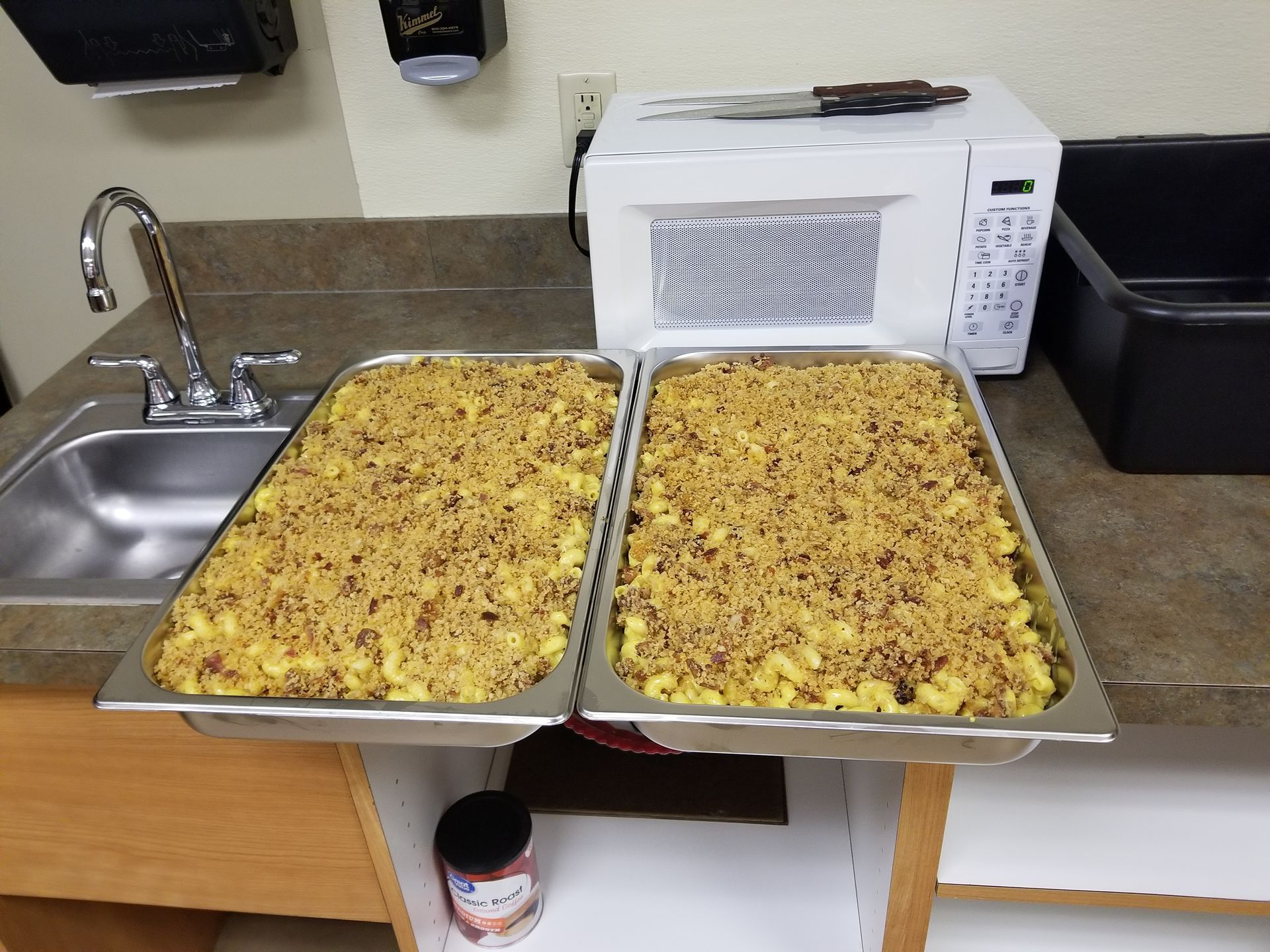 Two trays of cooked casserole on a kitchen counter beside a sink and microwave.