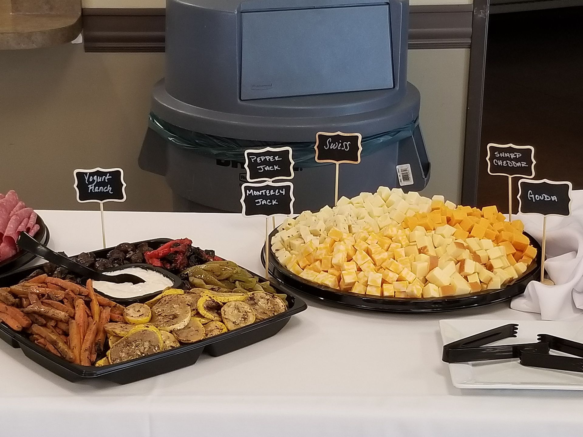 Buffet table with trays of food, including fries and pastries, labeled with small signs.