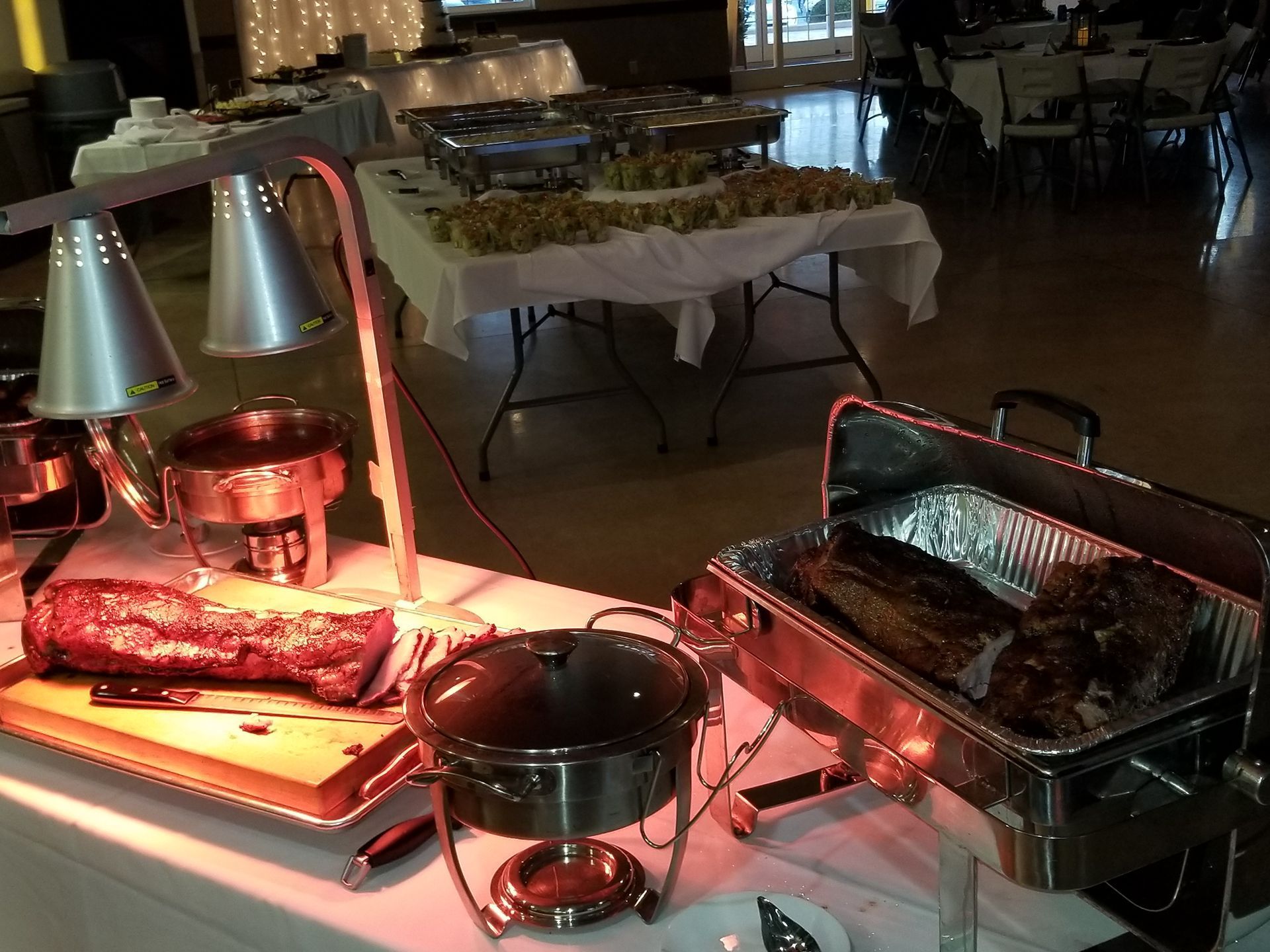 Buffet table with heat lamps, a roasting tray, and a covered chafing dish in a dim dining room