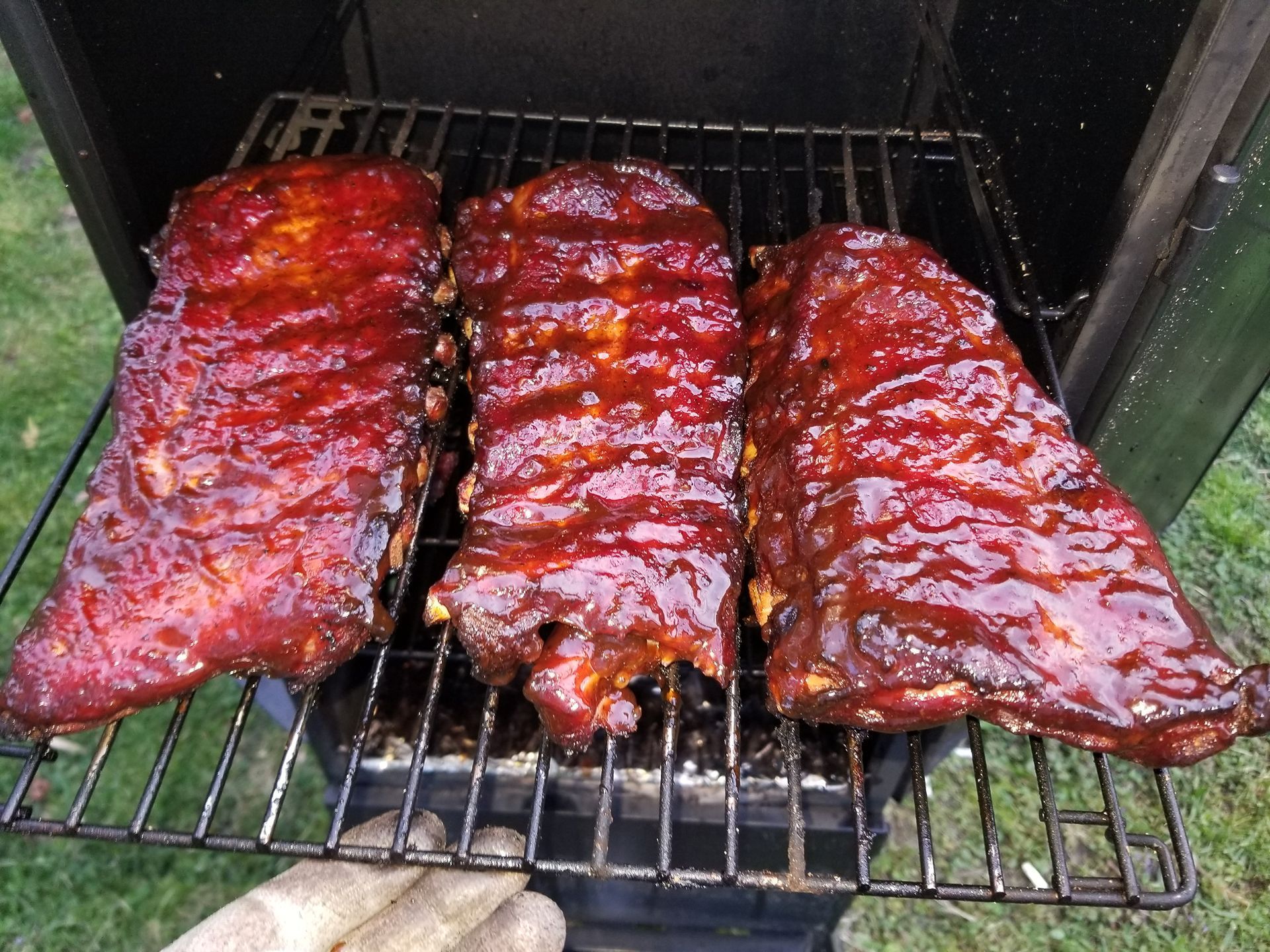 Three racks of glazed barbecue ribs on a grill, coated in shiny red sauce.