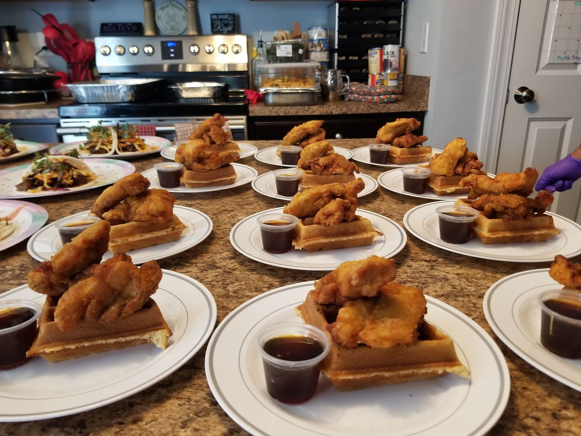 Plates of fried chicken and waffles with syrup arranged on a kitchen counter for serving