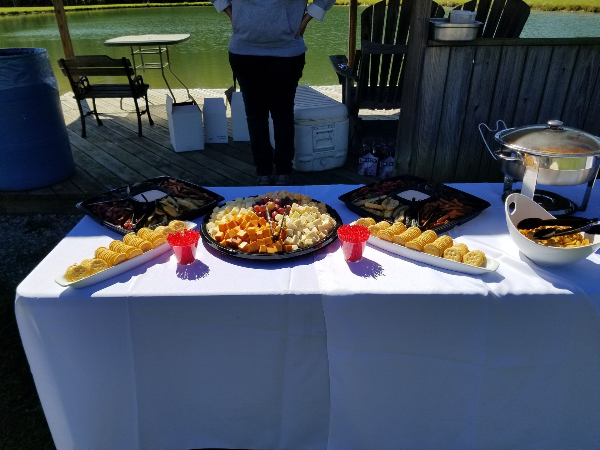 Outdoor buffet table with trays of food, red cups, and a stainless chafing dish on a patio