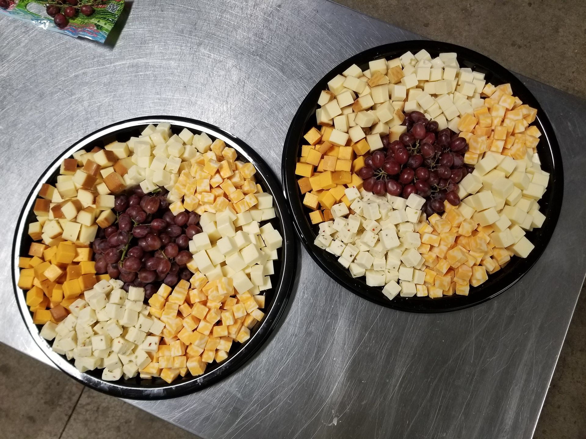 Two plates of cubed fruit and berries arranged in sections on a metal countertop