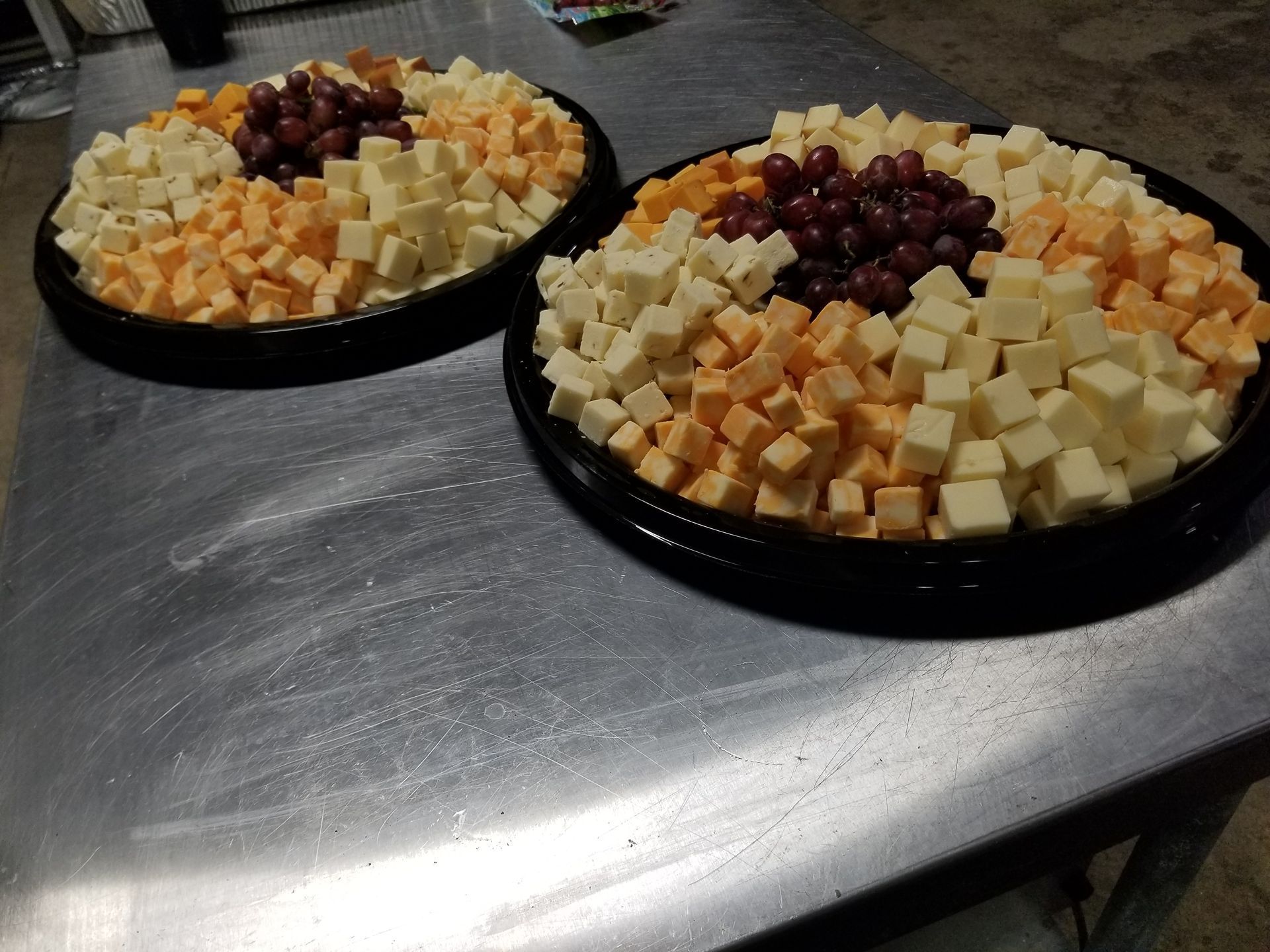 Two plates of cubed fruit and cheese on a table, topped with red grapes.