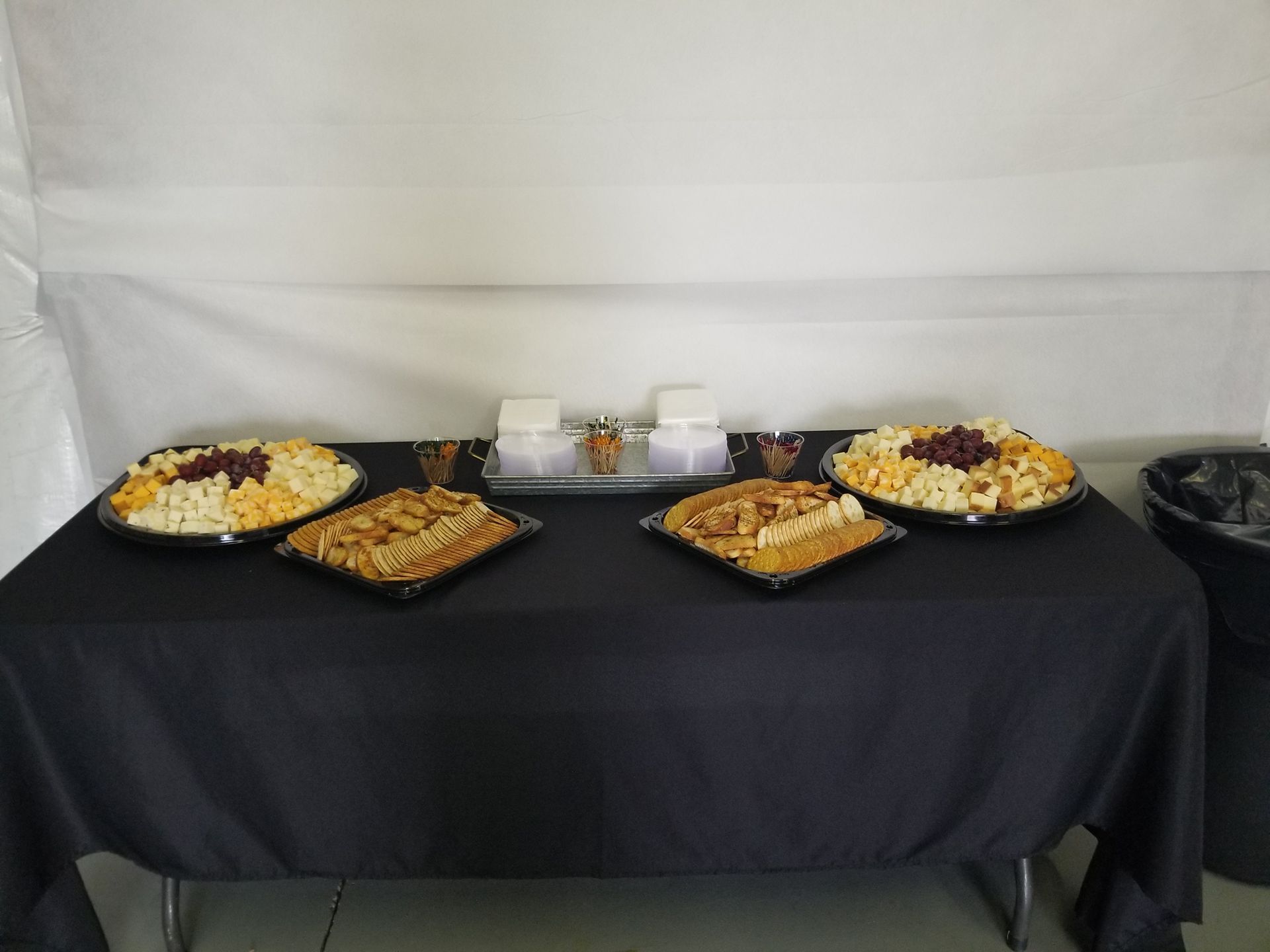 Buffet table with covered dishes and desserts on a black tablecloth against a white backdrop