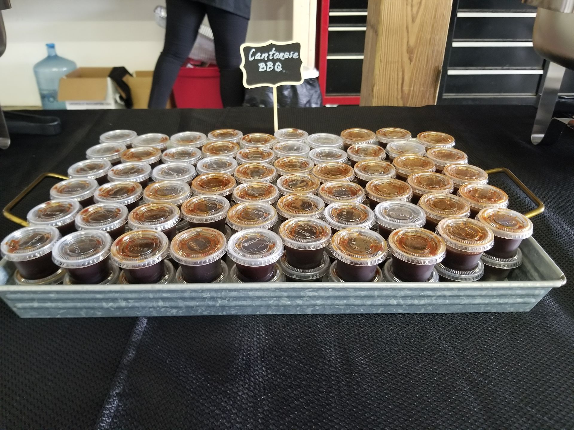 Tray of small dessert cups at a market stall with a handwritten sign in the background