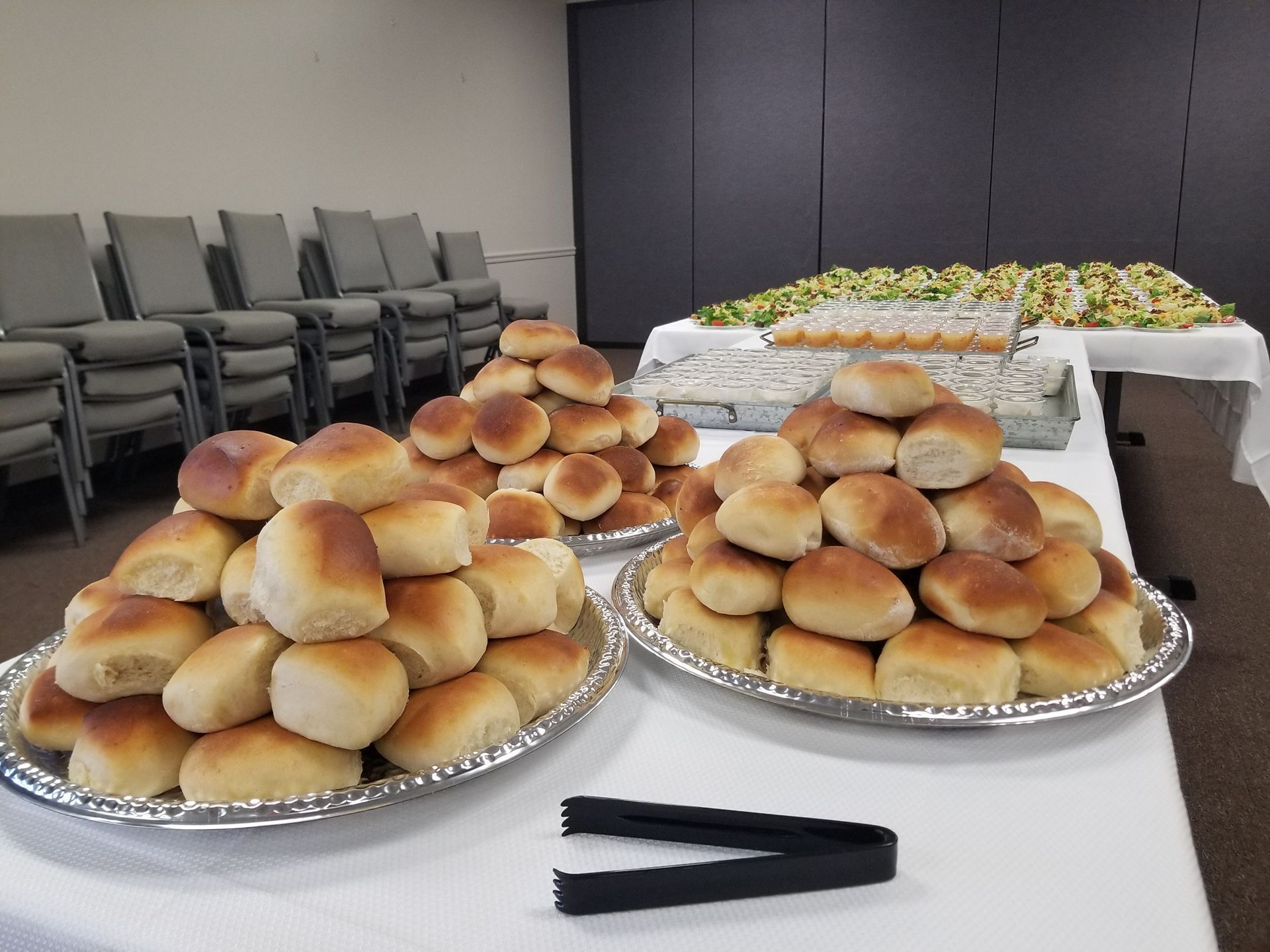 Trays of dinner rolls on a table in a meeting room, with chairs stacked in the background.
