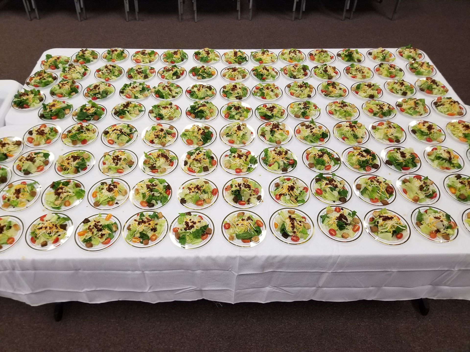 Rows of small bowls filled with salad on a white tablecloth at a catered event