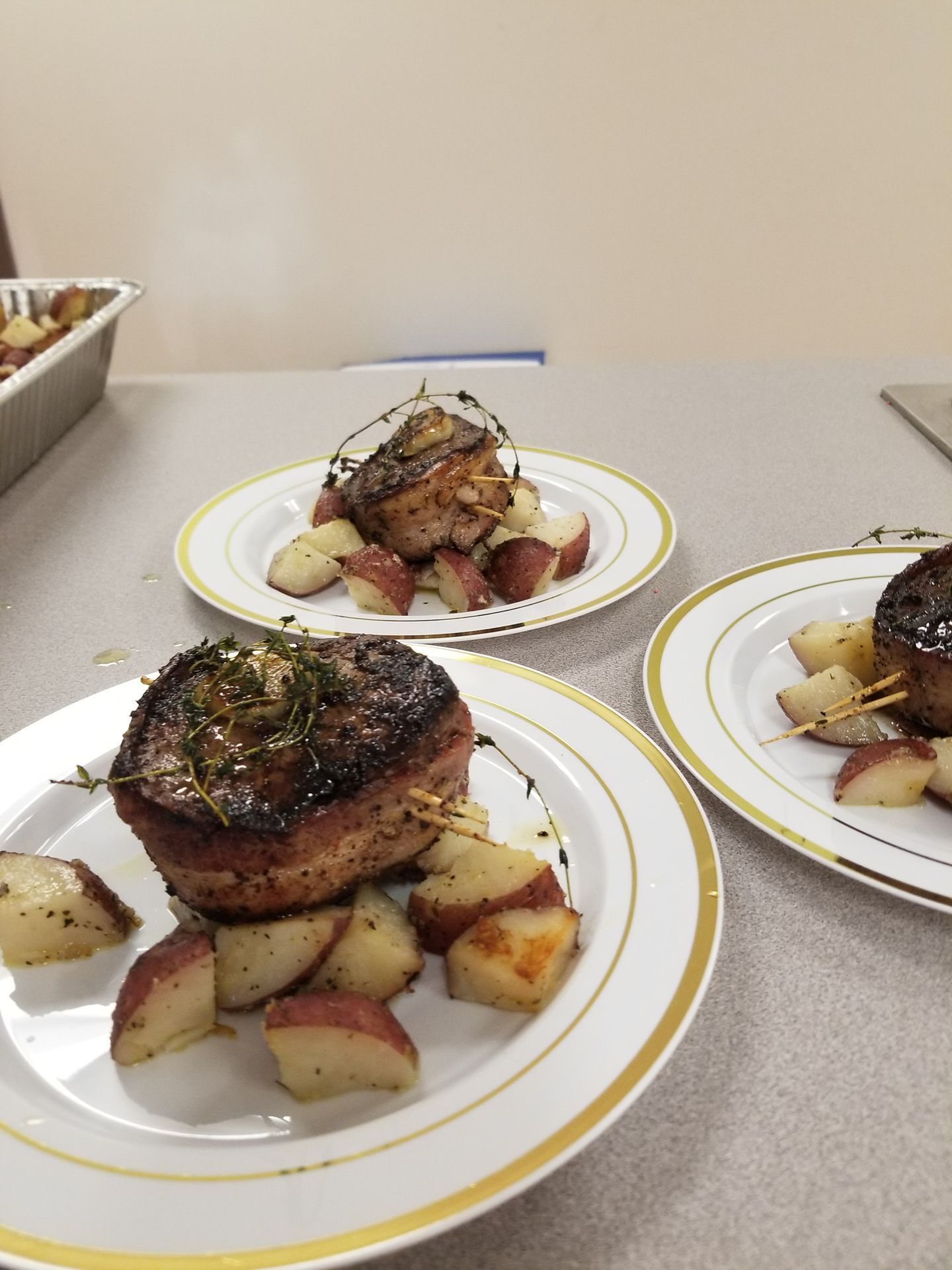 Plated roasted meat with diced potatoes on a white table, with a second plate in the background