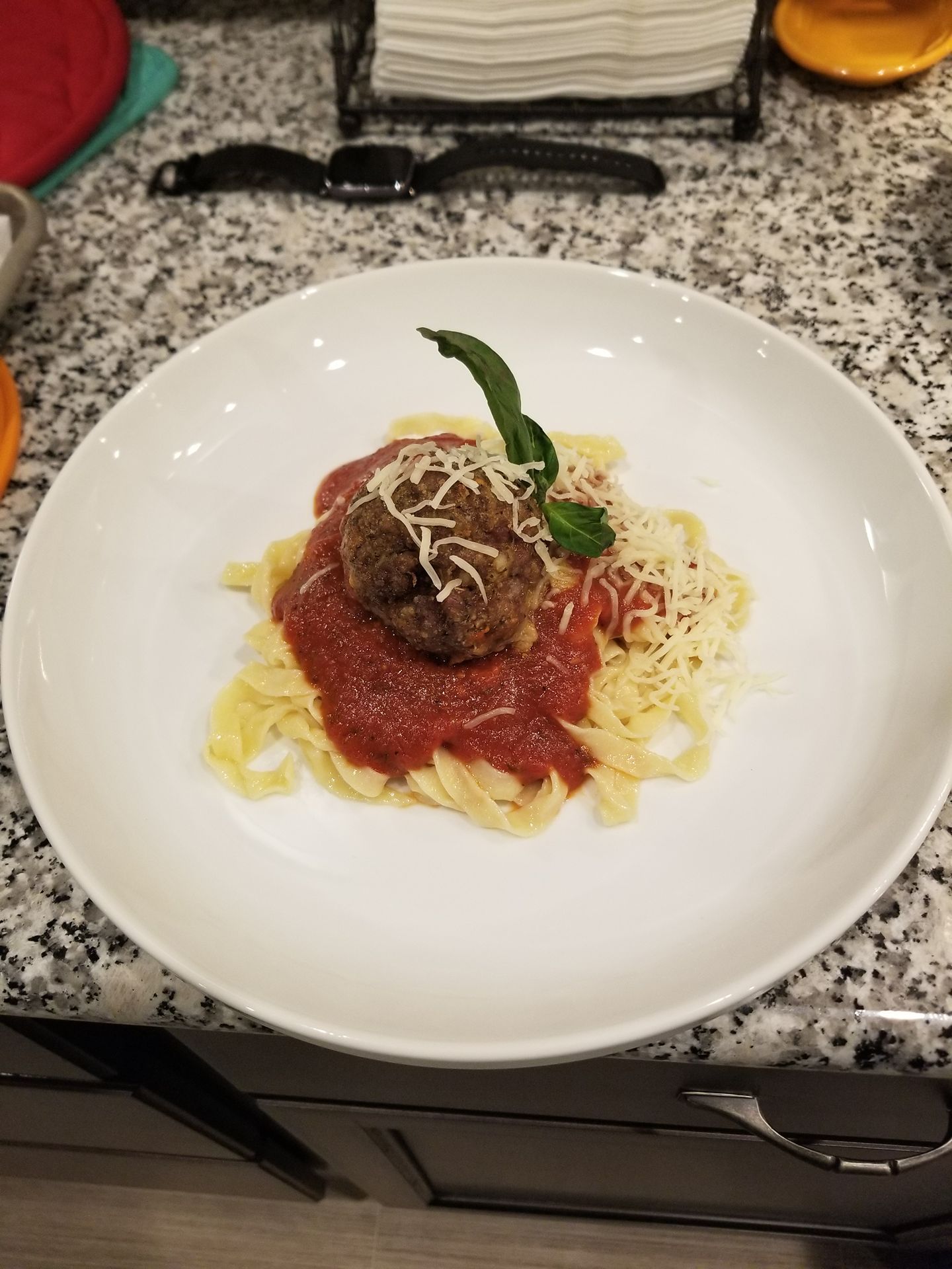 Plated pasta with tomato sauce and meatball, topped with herbs and grated cheese