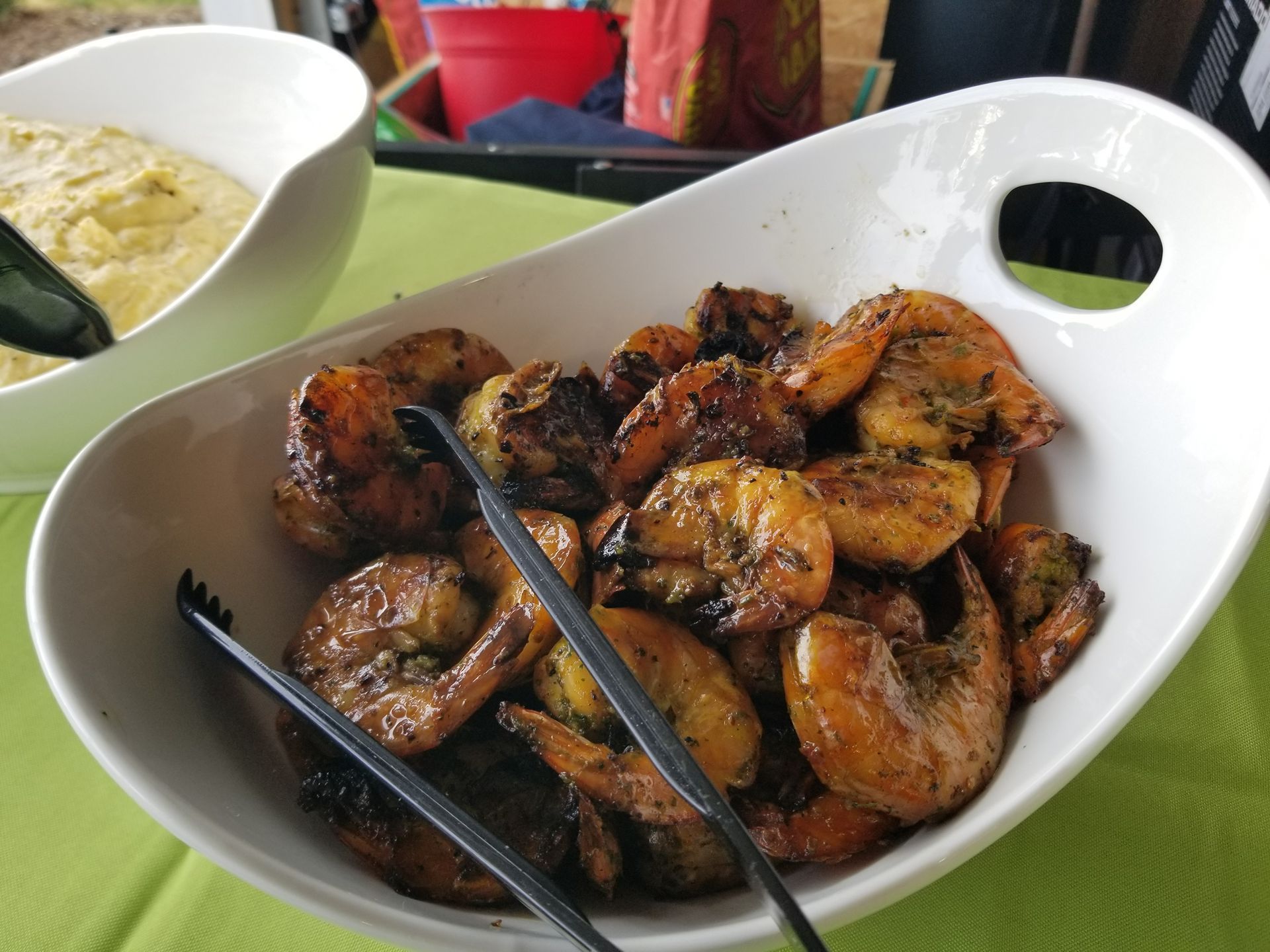 Tray of grilled chicken pieces on a table with a bowl of side dish in the background