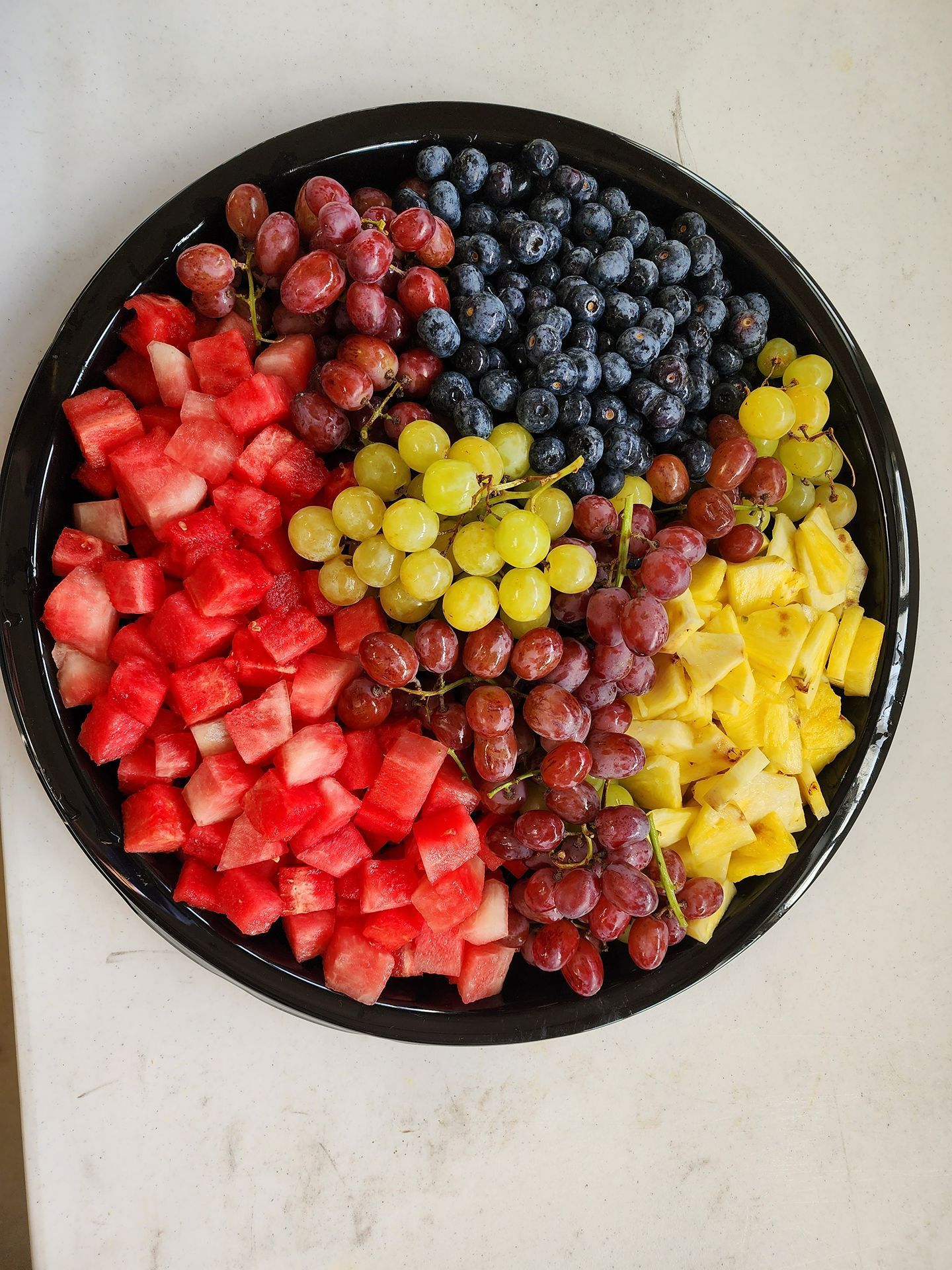 Colorful fruit platter with strawberries, blueberries, grapes, and pineapple arranged in sections