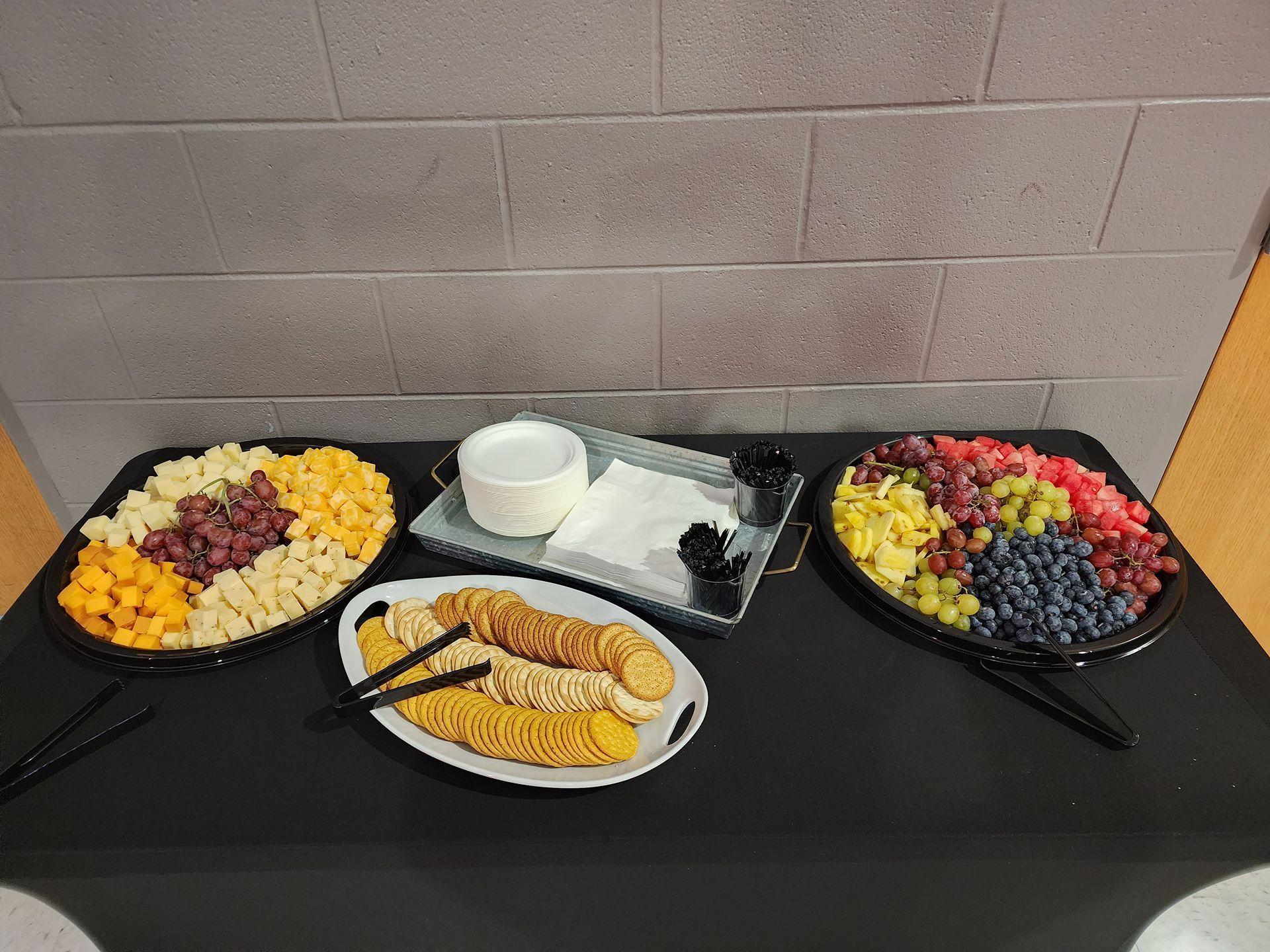 Fruit and pastry platters on a black counter, with bowls and a white serving dish against a tiled wall