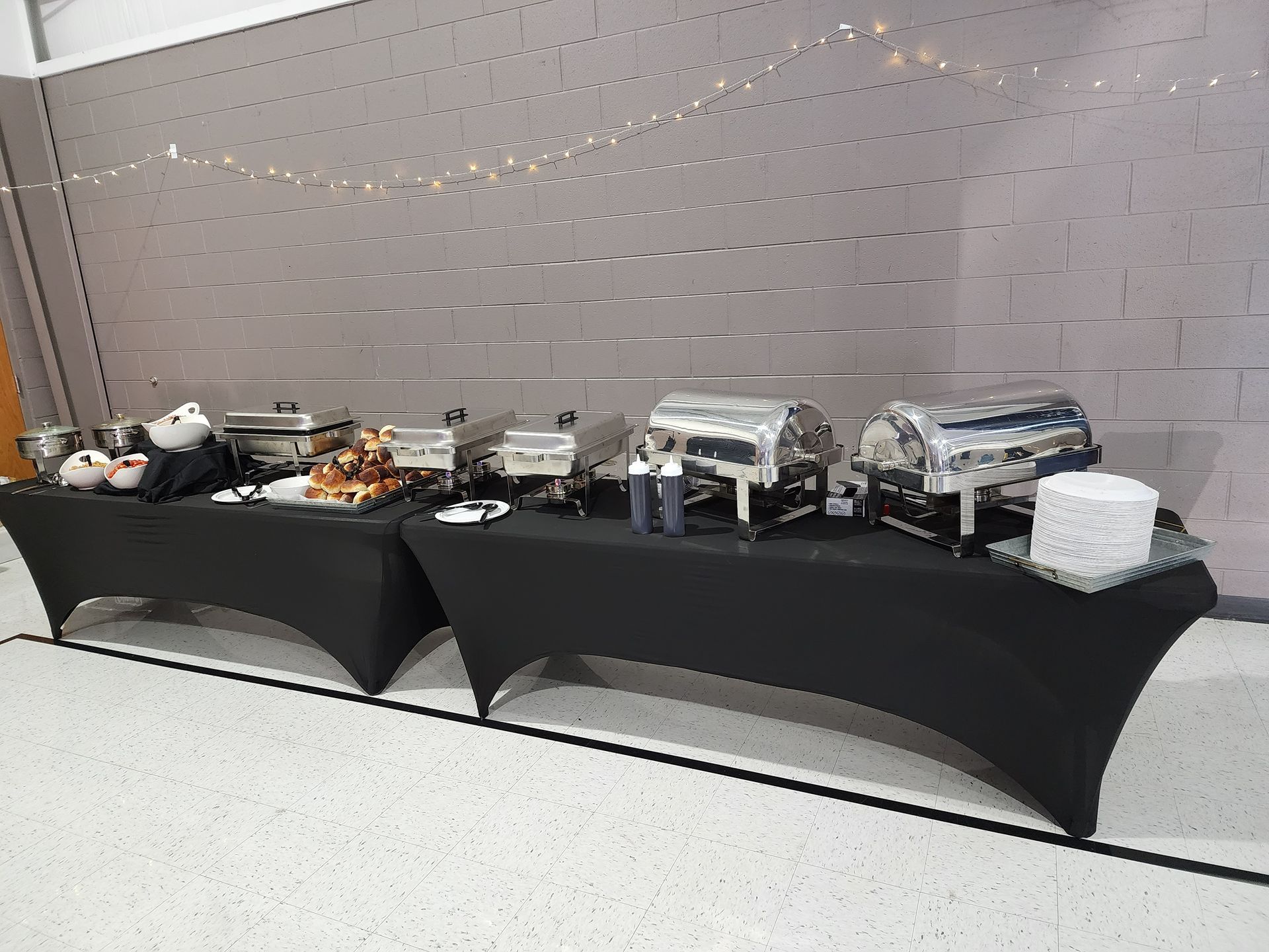 Buffet table with covered trays and food dishes against a gray wall in a banquet-style setting