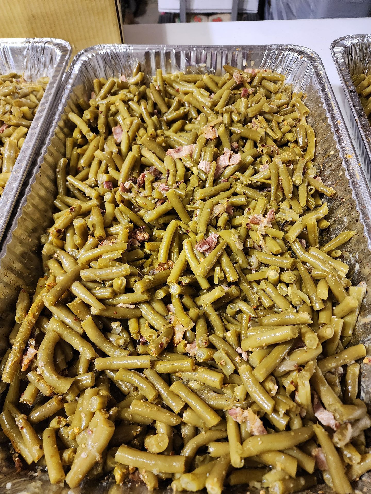 Tray of green pasta salad with chopped pink bits in a foil pan