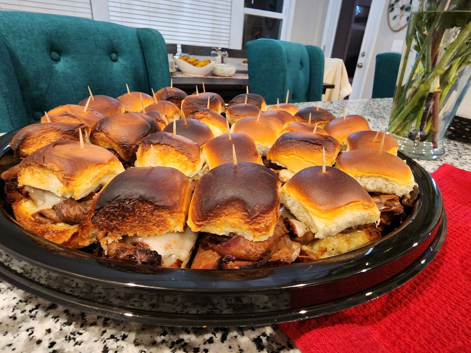 Tray of toasted slider sandwiches on a dining table with teal chairs in the background