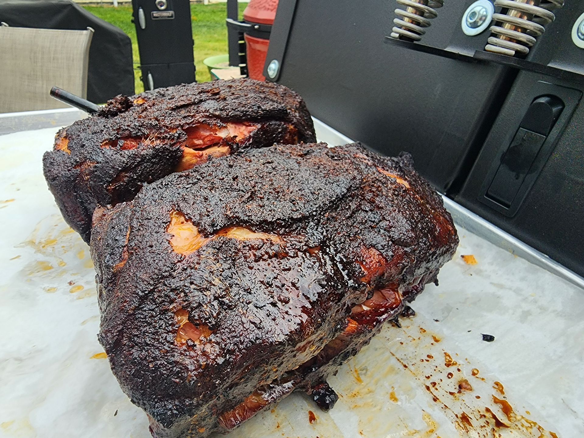 Two charred smoked meat cuts on white butcher paper, with a barbecue grill in the background