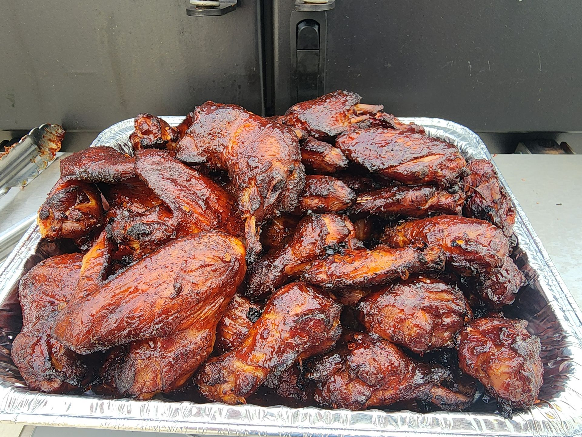 Tray piled high with glazed, charred chicken wings on a foil-lined grill tray