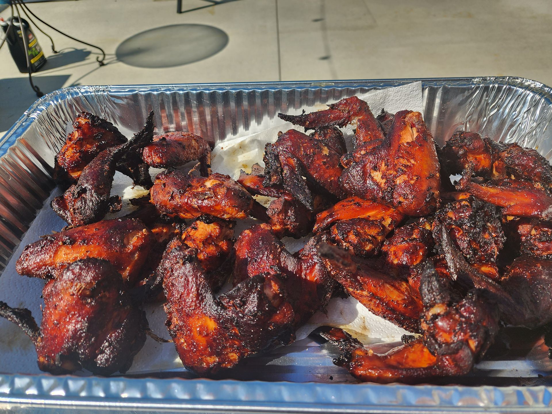 Tray of dark glazed grilled chicken wings and pieces in a foil pan