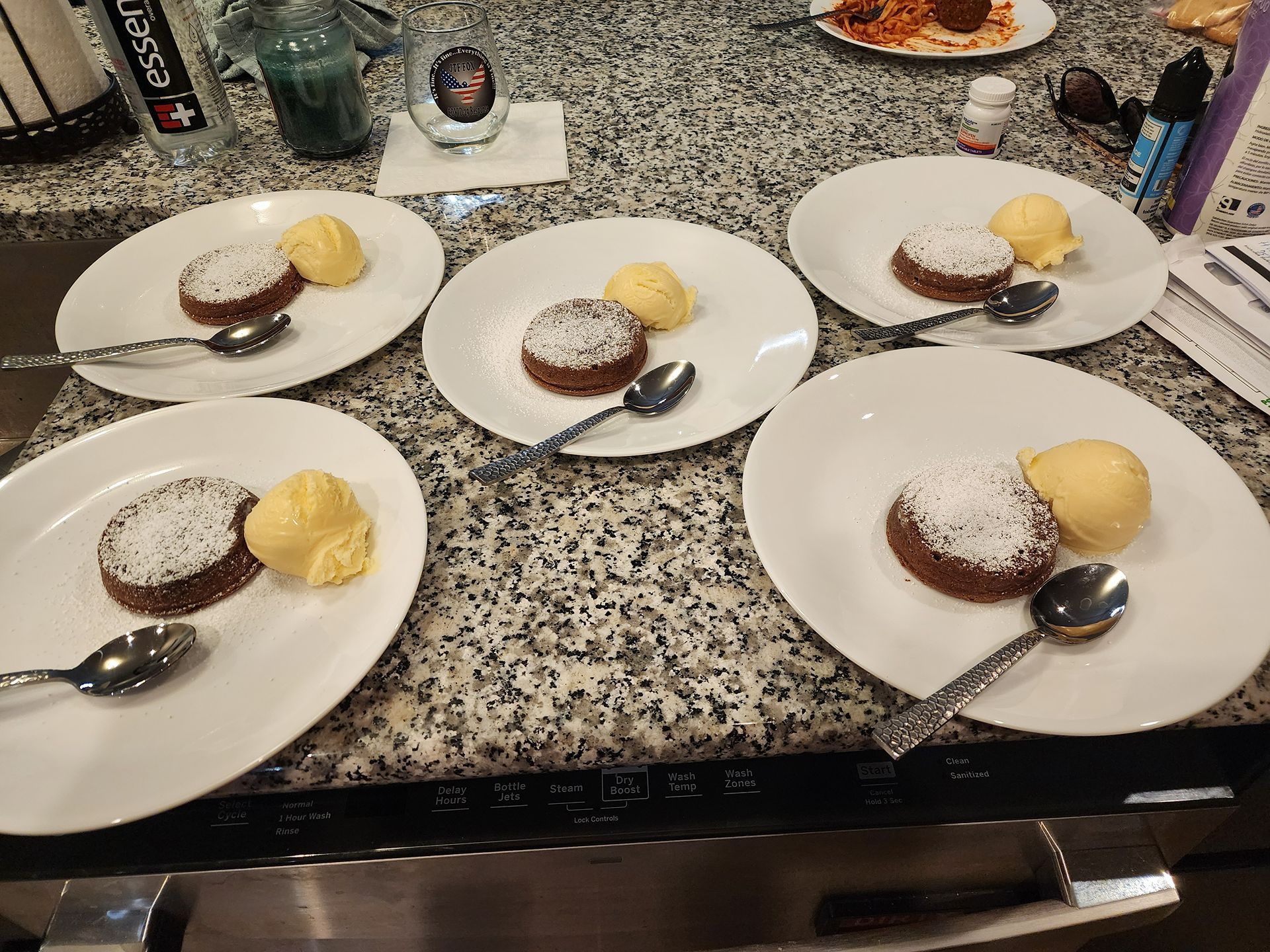 Four dessert plates on a speckled countertop, each with cake, yellow scoop, and a spoon.