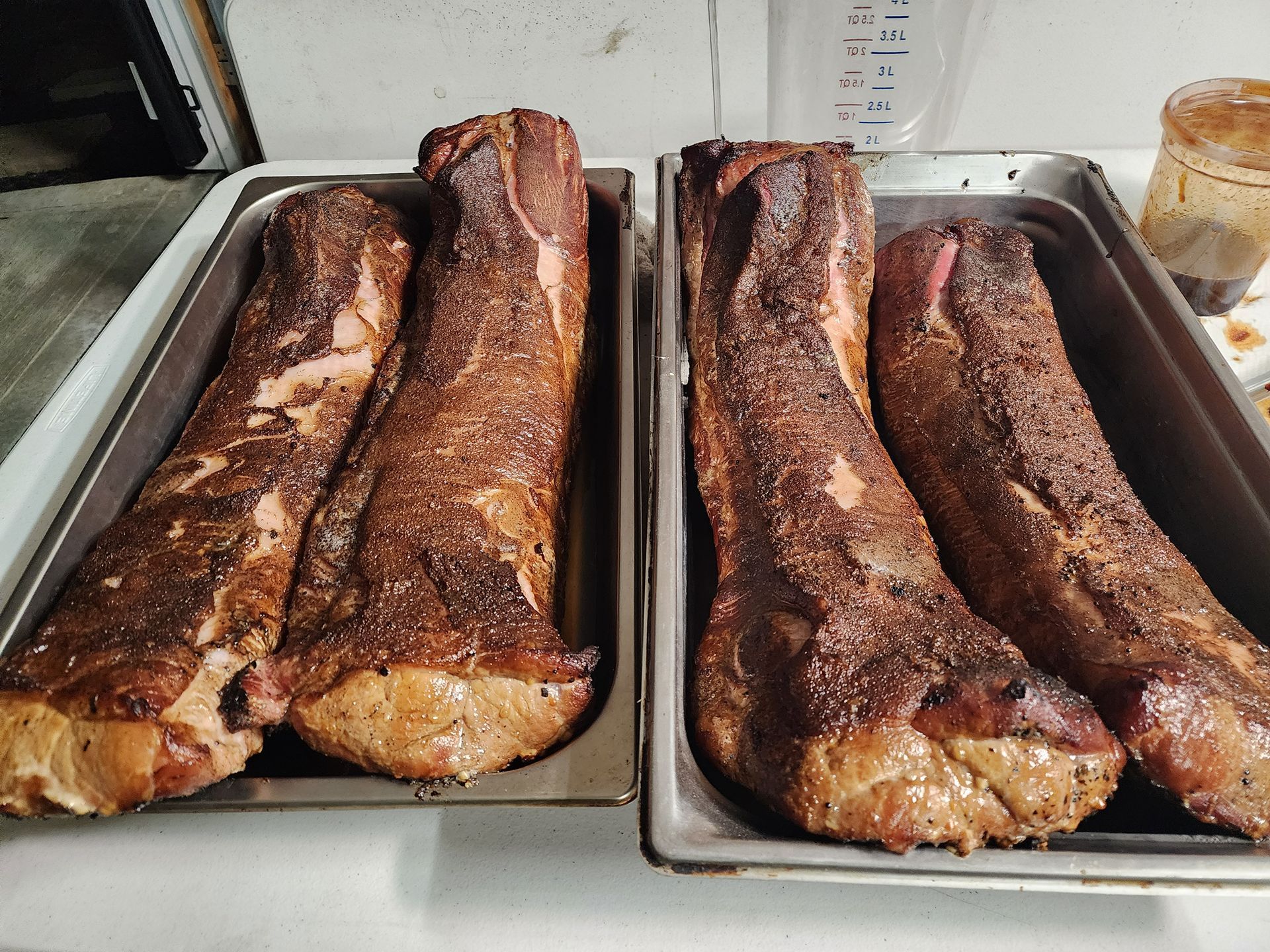 Two trays of roasted meat on a kitchen counter, browned and glazed on top.