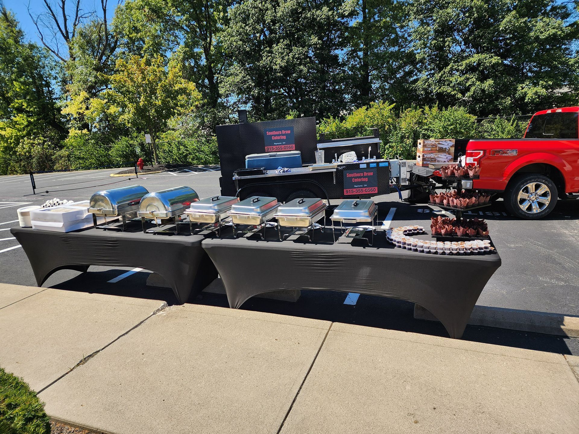 Outdoor table display of assorted items at a parking lot, with a red truck and trees in the background