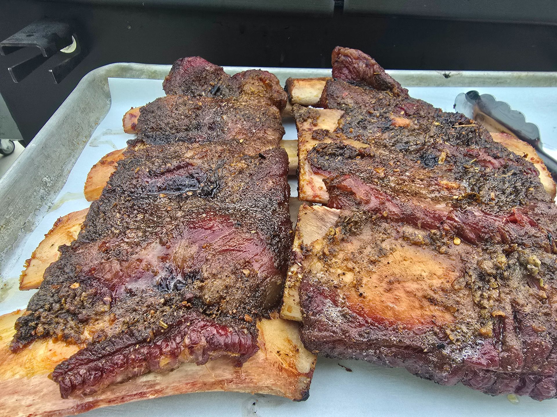 Two slabs of seasoned ribs cooking on a foil-lined baking tray