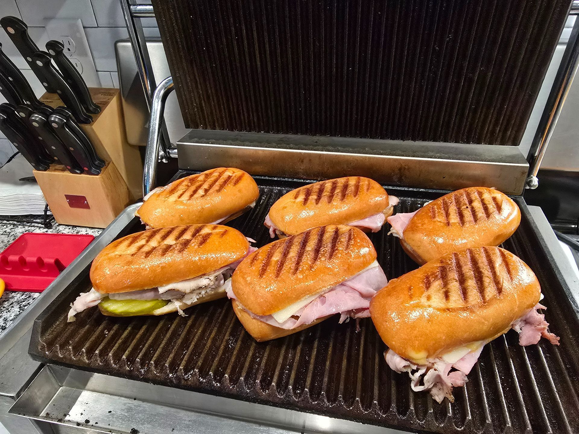 Panini sandwiches grilling on a press, with toasted bun tops and melted fillings visible