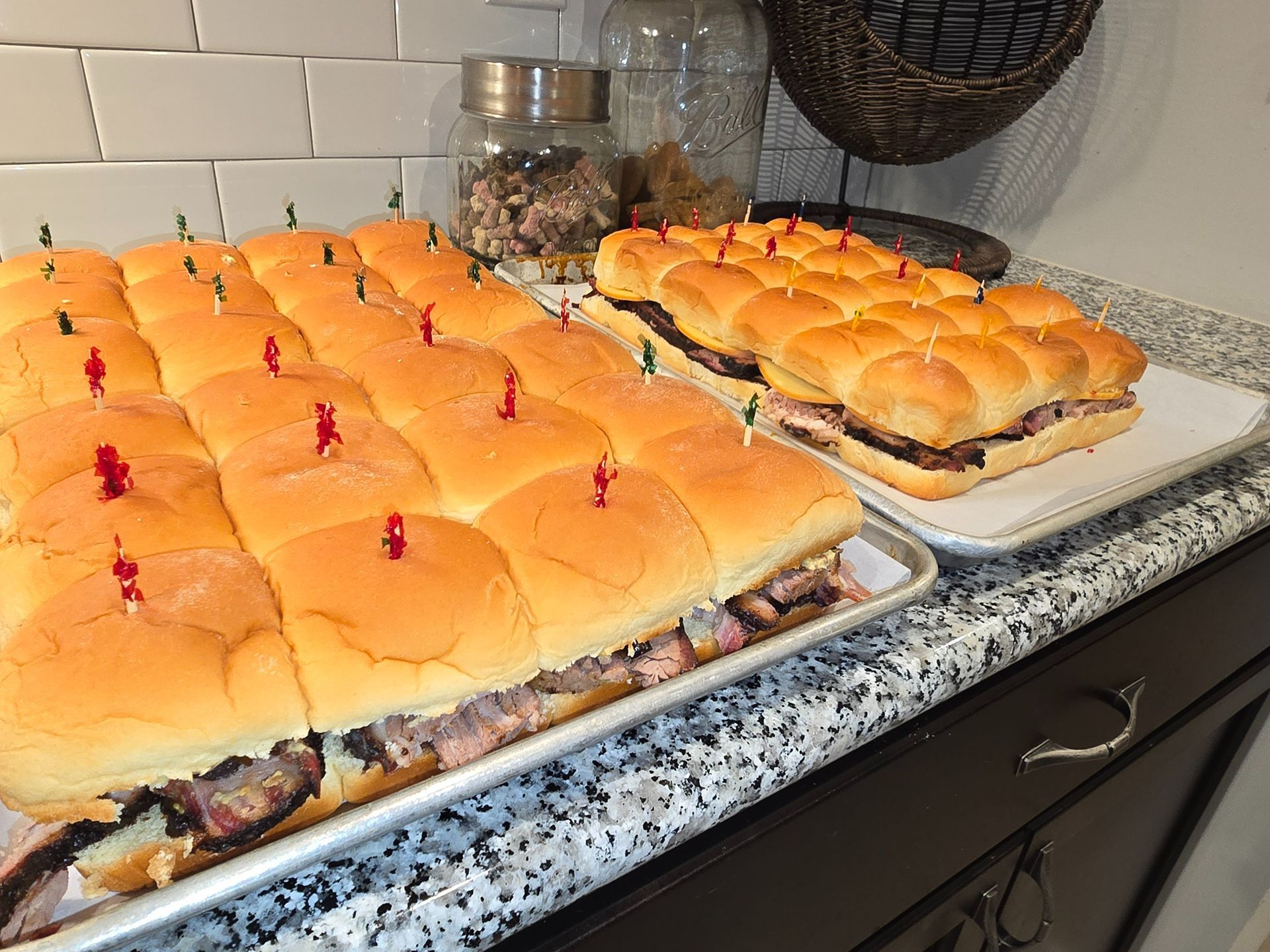 Tray of pulled pork sandwich sliders on a kitchen counter, topped with red toothpicks.