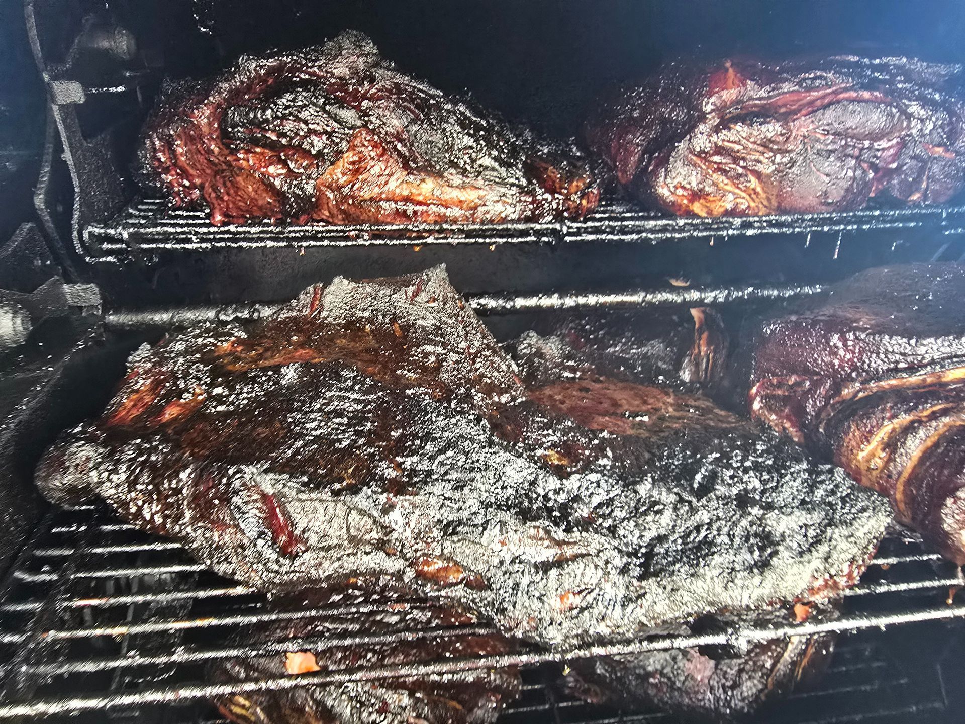 Brisket and ribs smoking on a grill, charred and glossy, in a barbecue smoker