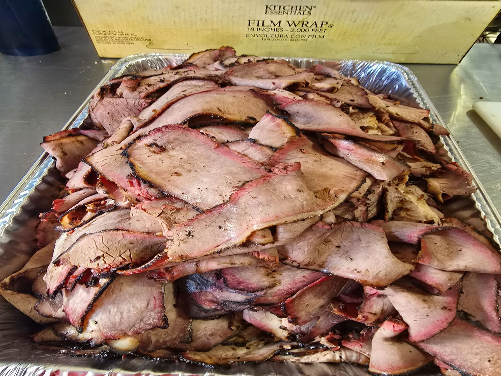 Tray piled high with sliced smoked meat, likely roast beef, at a deli counter