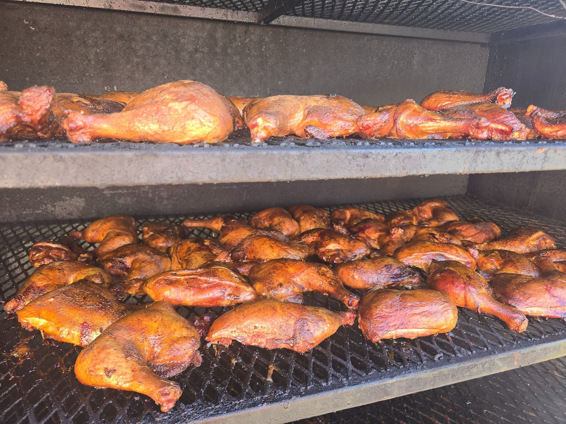 Rows of smoked chicken pieces cooking in a smoker, with golden-brown meat on two racks.