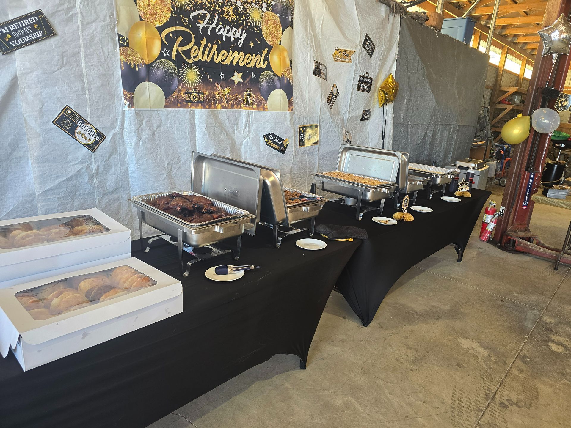 Buffet dessert table with covered trays, black tablecloth, and decorative sign in a banquet hall