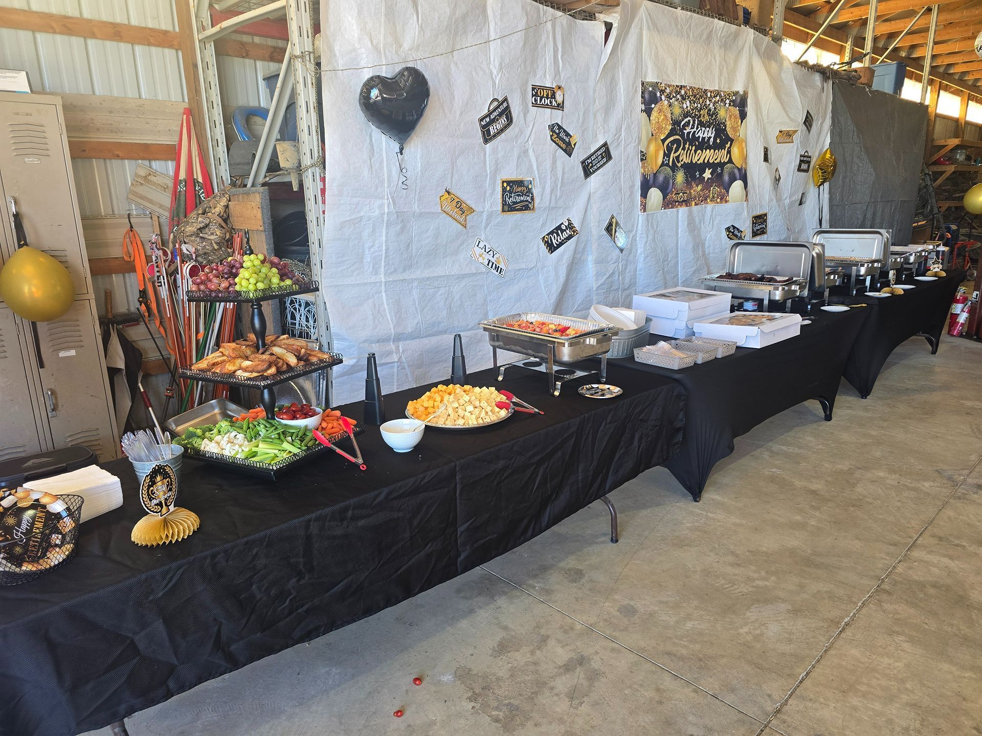 Buffet table with black tablecloths, trays of food, and drinks set up in a warehouse-like event space