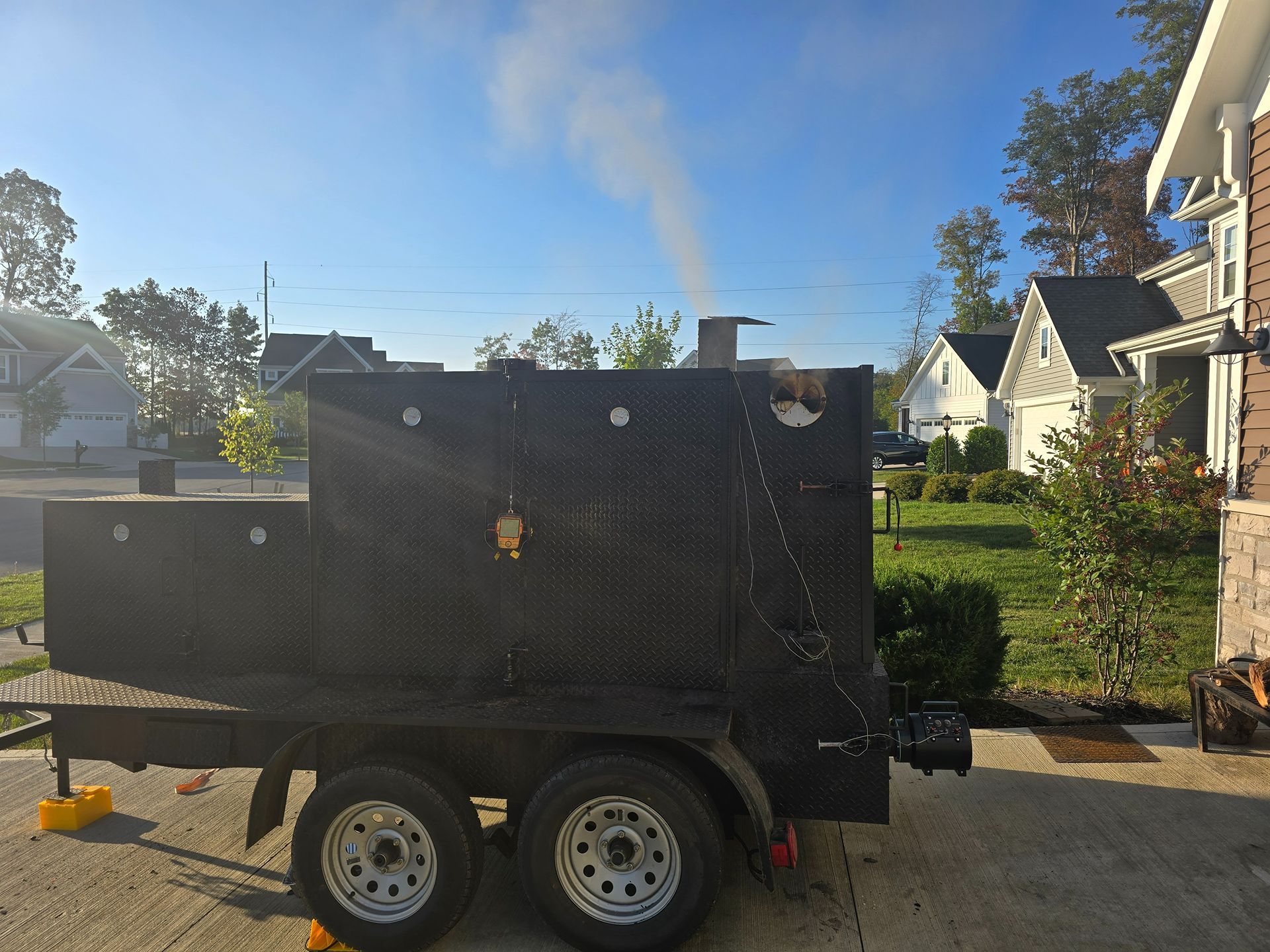 Black enclosed trailer parked on a residential street with a plume of smoke rising behind it.