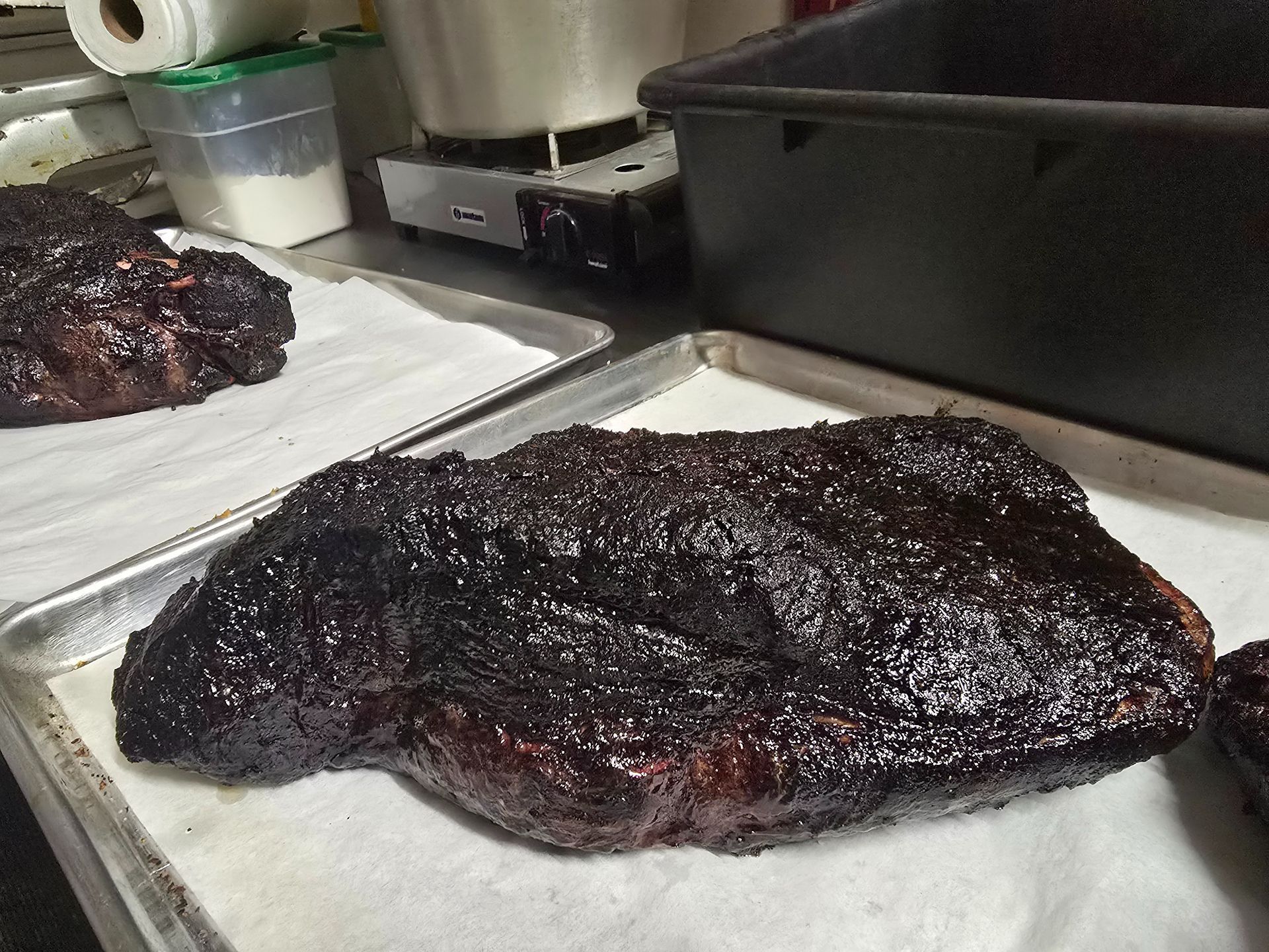 Smoked brisket on a metal tray in a kitchen prep area