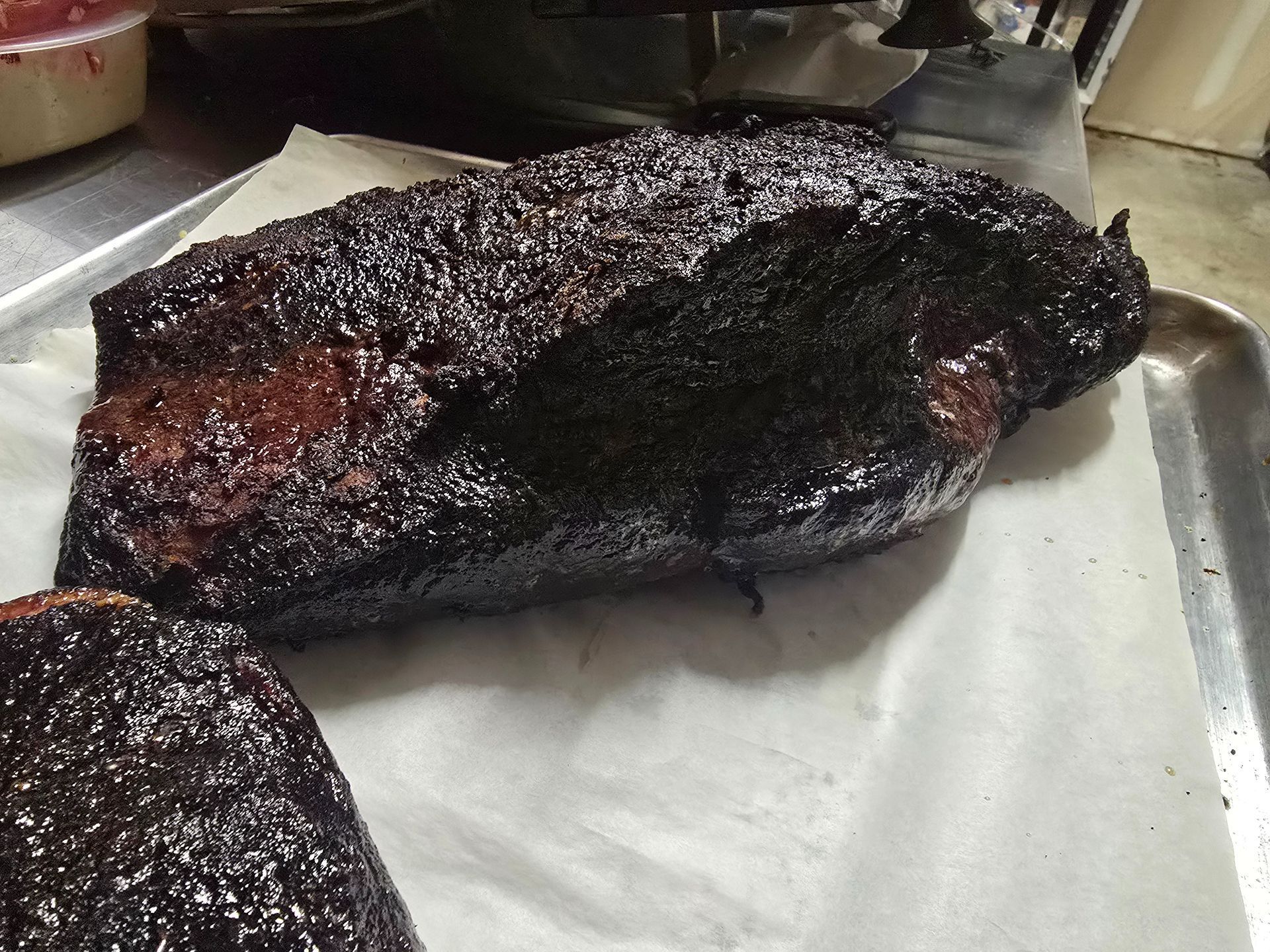 Charred smoked meat brisket on a metal tray lined with white paper