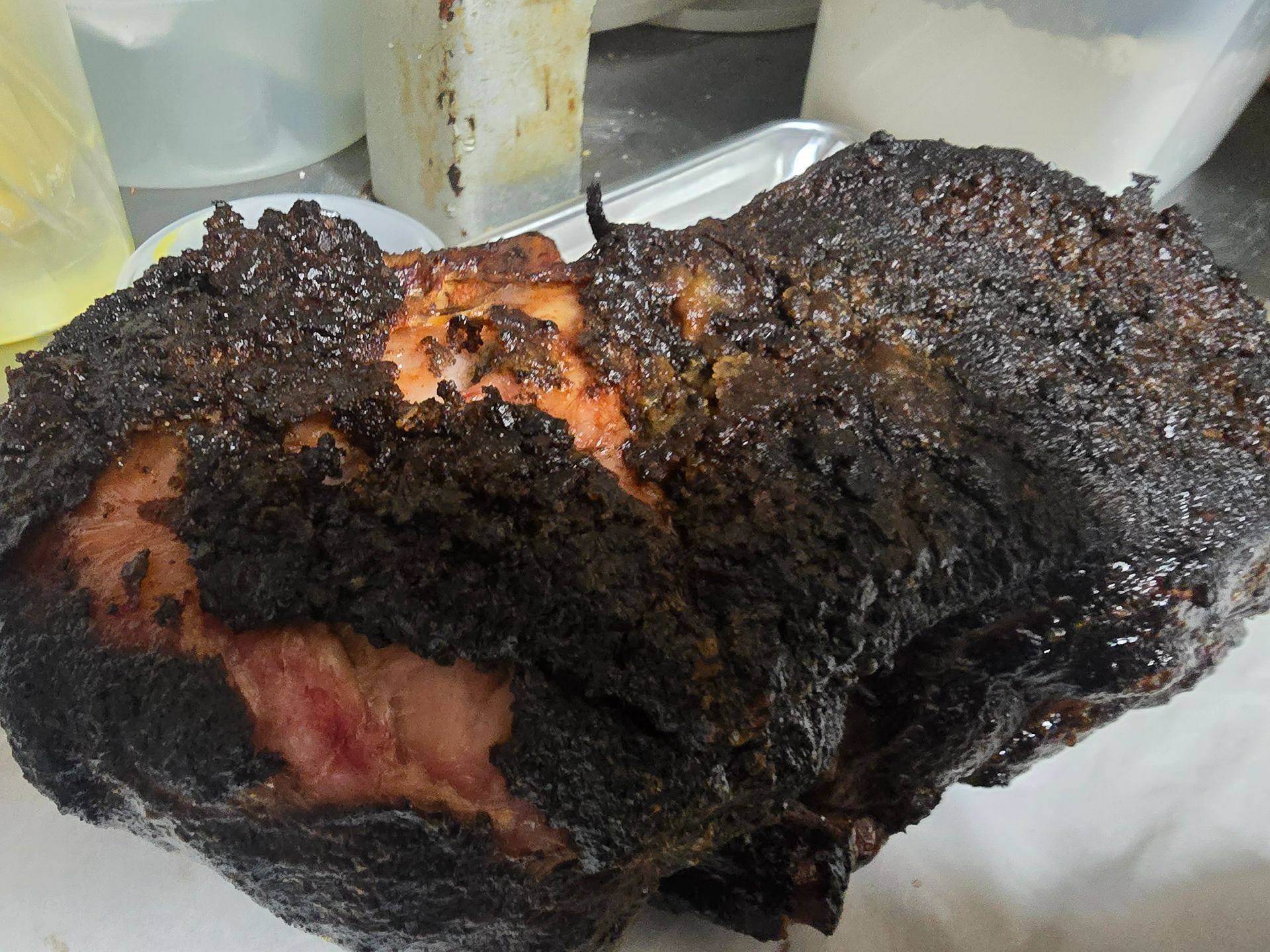 Charred, blackened piece of cooked meat on a plate, with a pink center visible through the crust