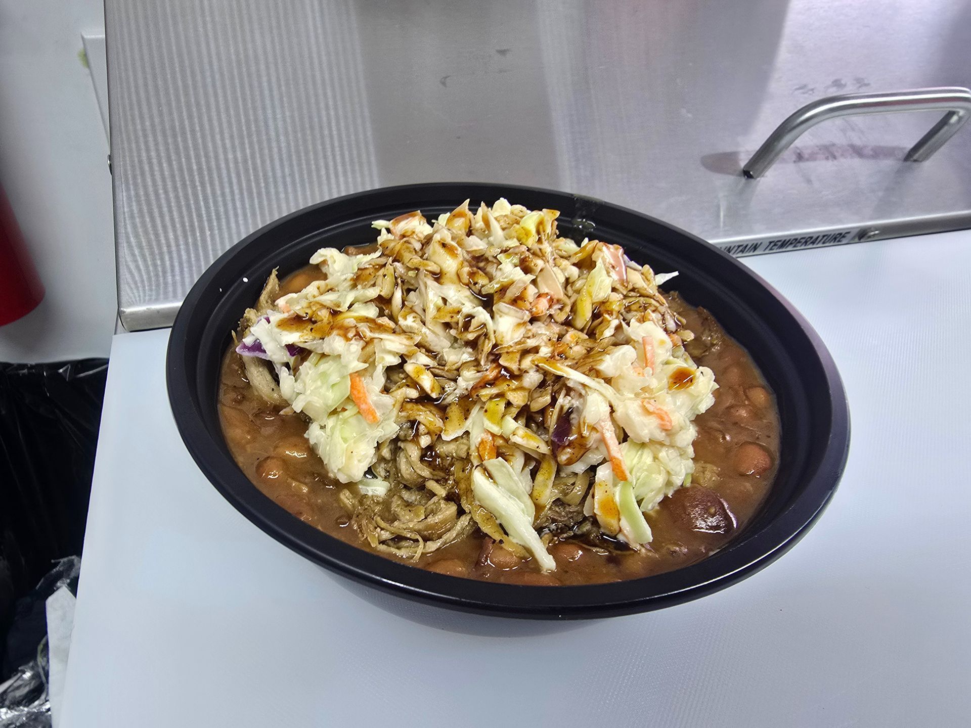 Bowl of stew topped with shredded vegetables on a metal countertop in a kitchen