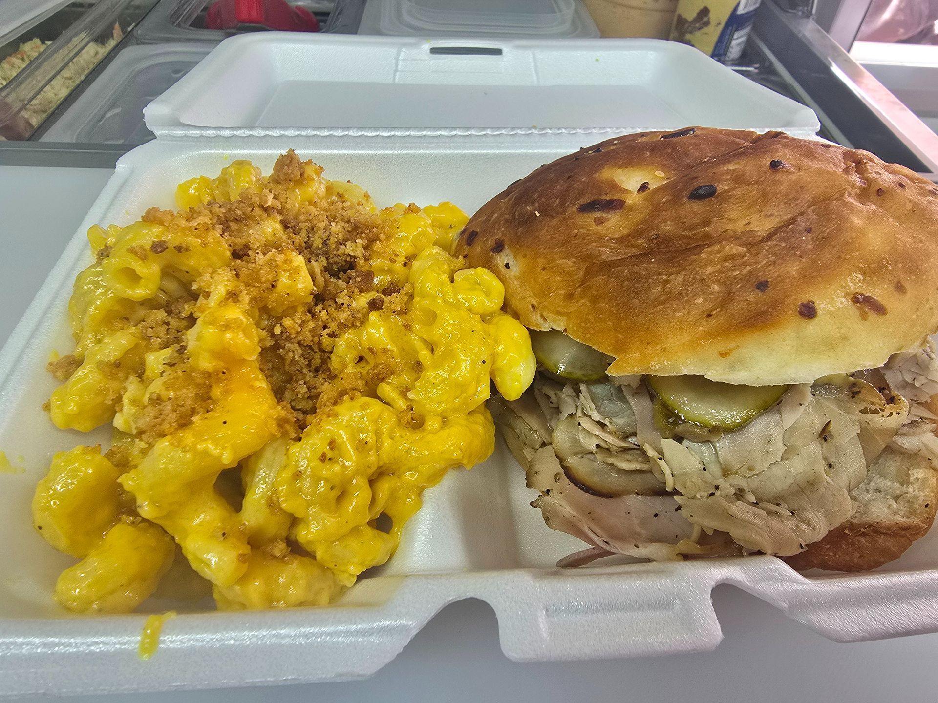 Takeout container with macaroni and cheese and a roasted pork sandwich on a bun
