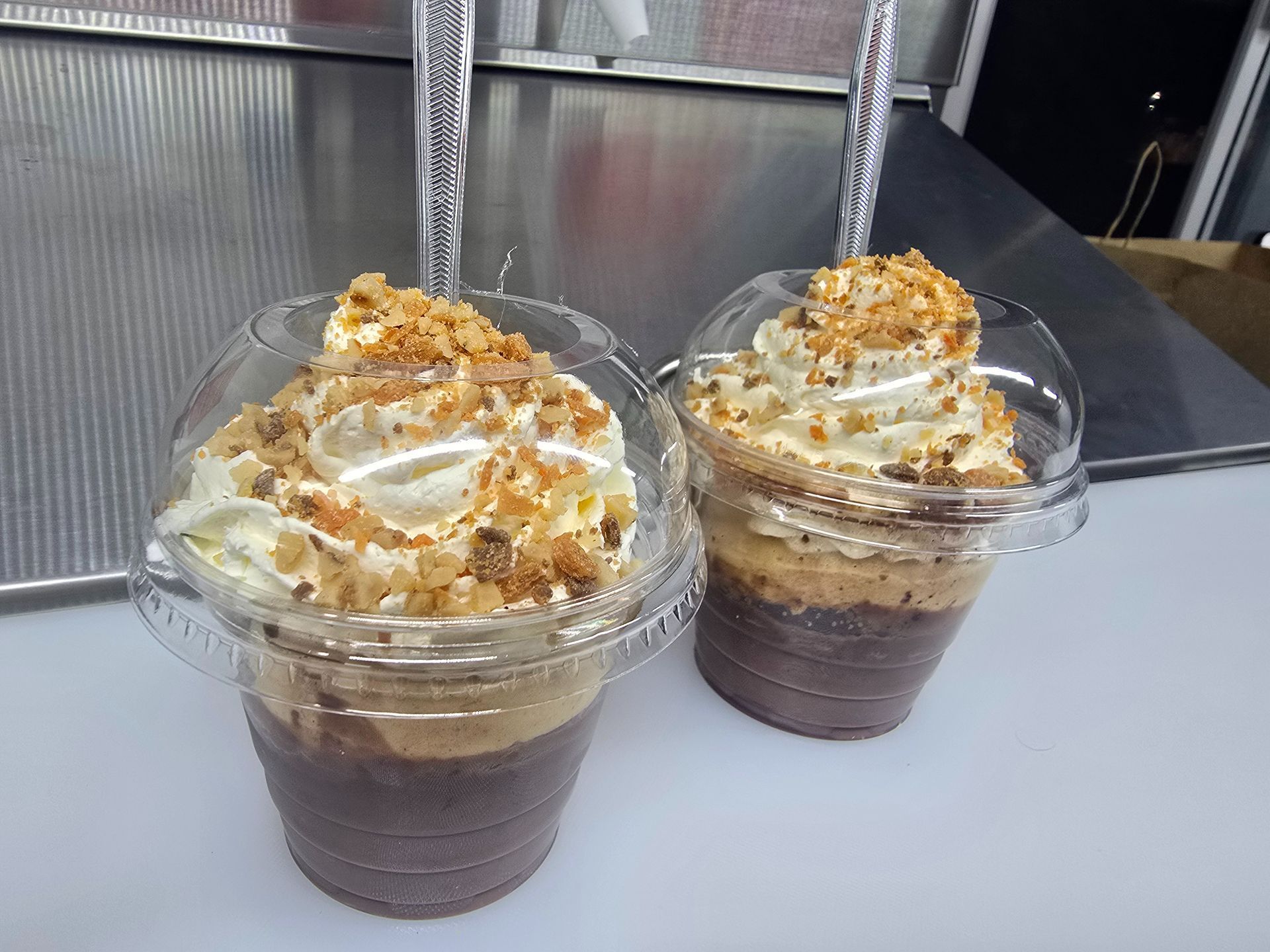 Two chocolate dessert cups topped with whipped cream and caramel bits in clear plastic cups