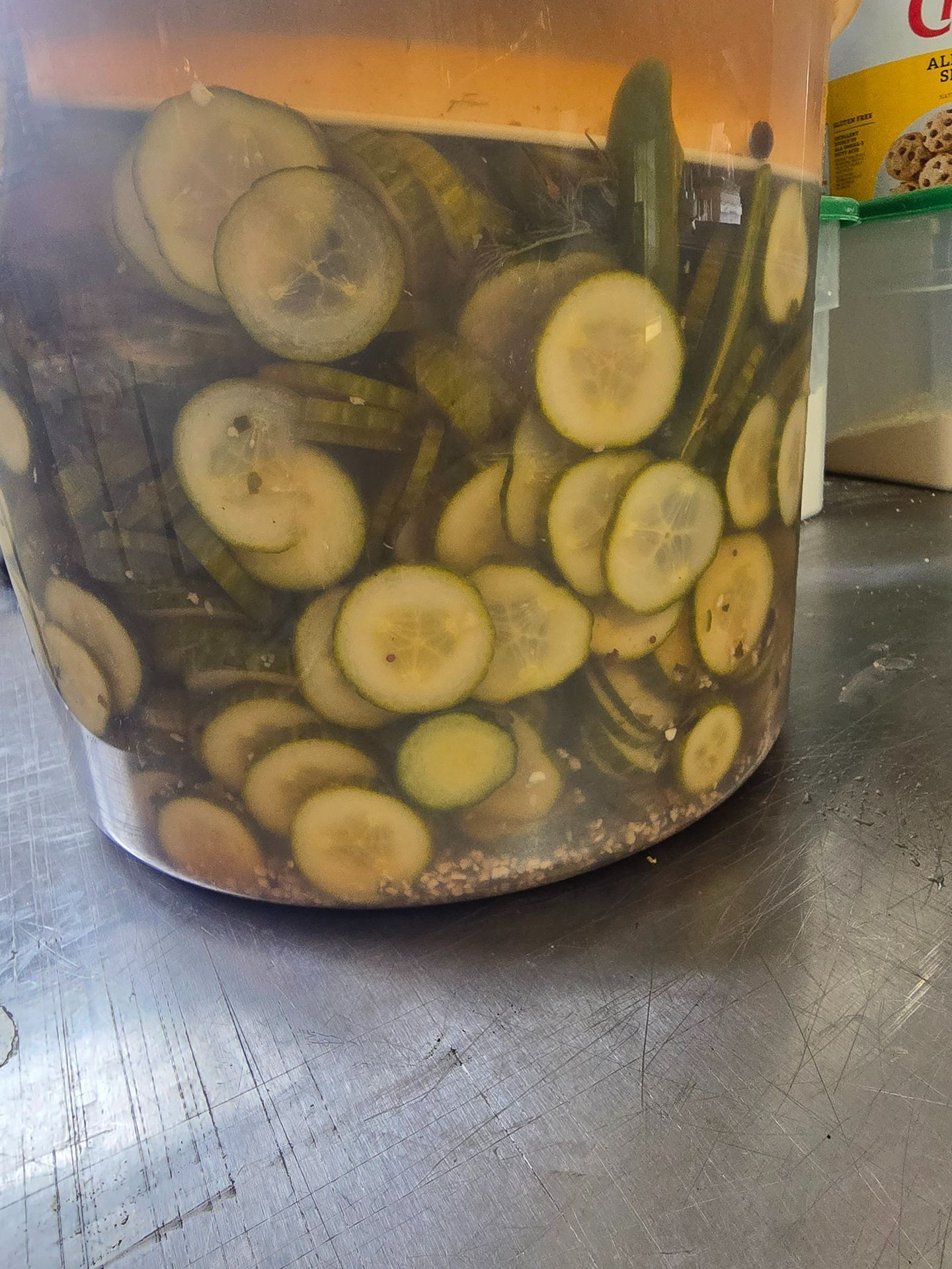 Jar of sliced cucumbers in brine on a dark countertop.
