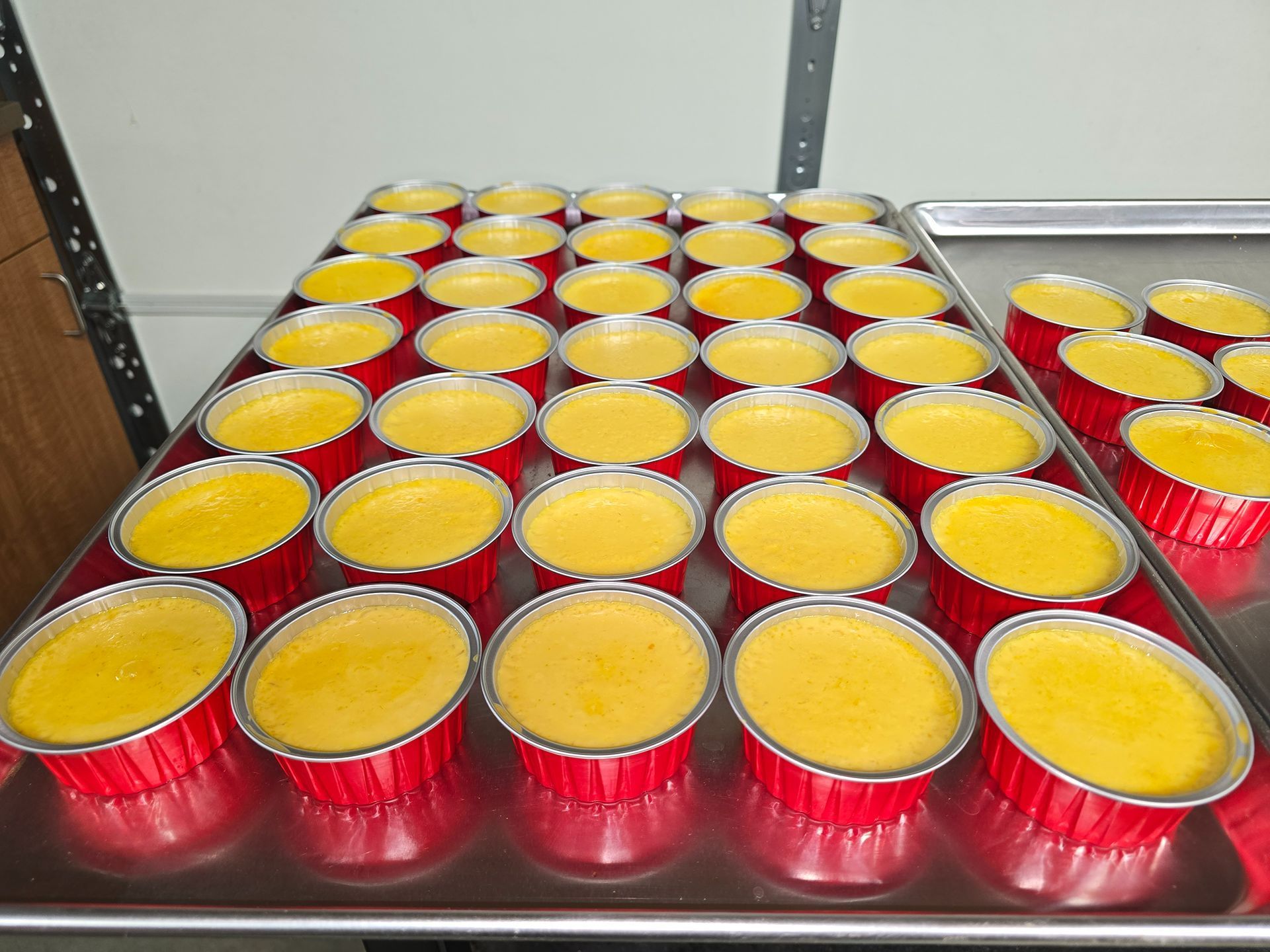 Rows of red cups filled with yellow batter on a tray, ready for baking
