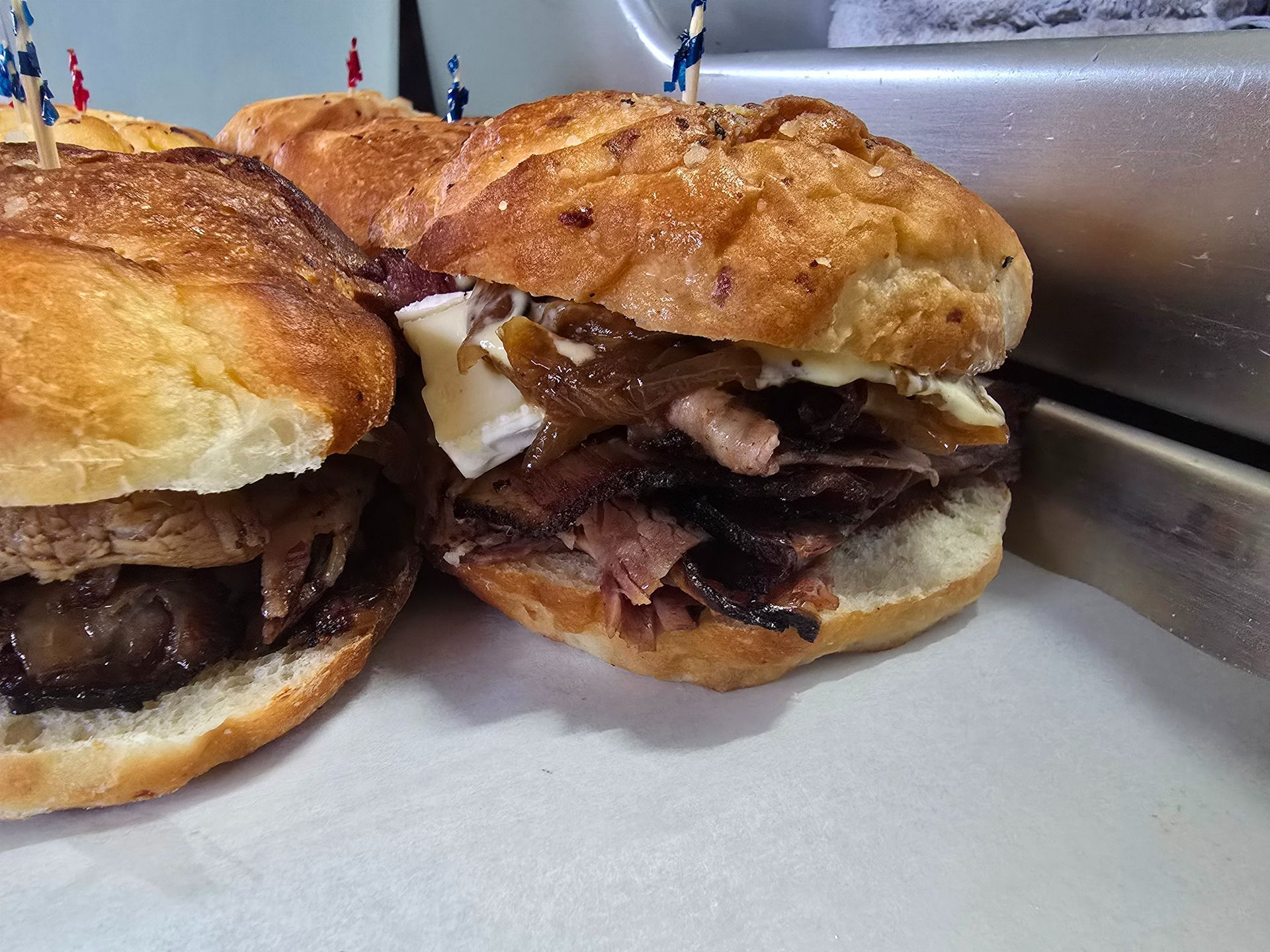 Two stacked sandwiches with toasted buns and meat on a counter, close-up.