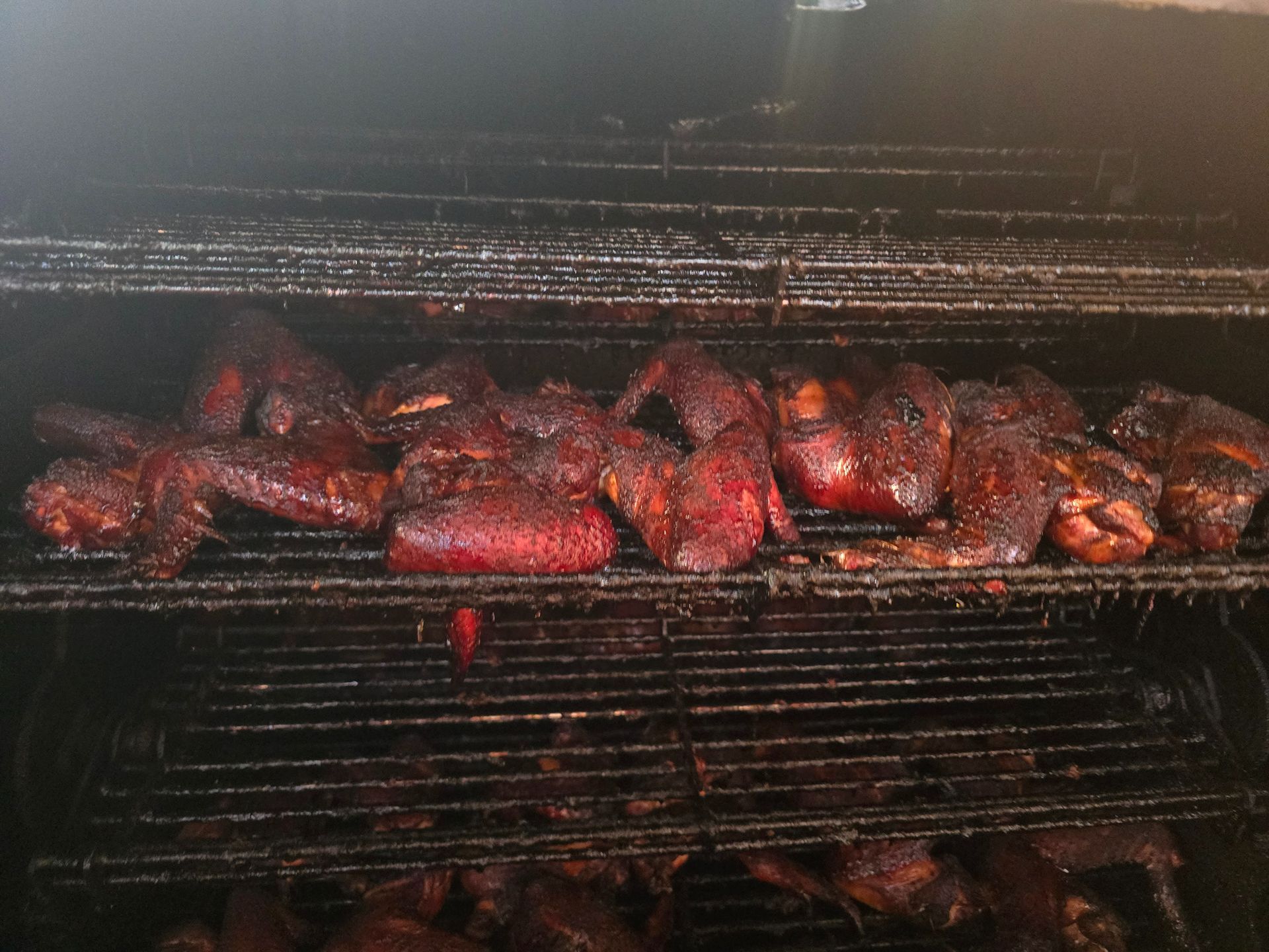Smoked meat and chicken sizzling on grill grates inside a barbecue smoker
