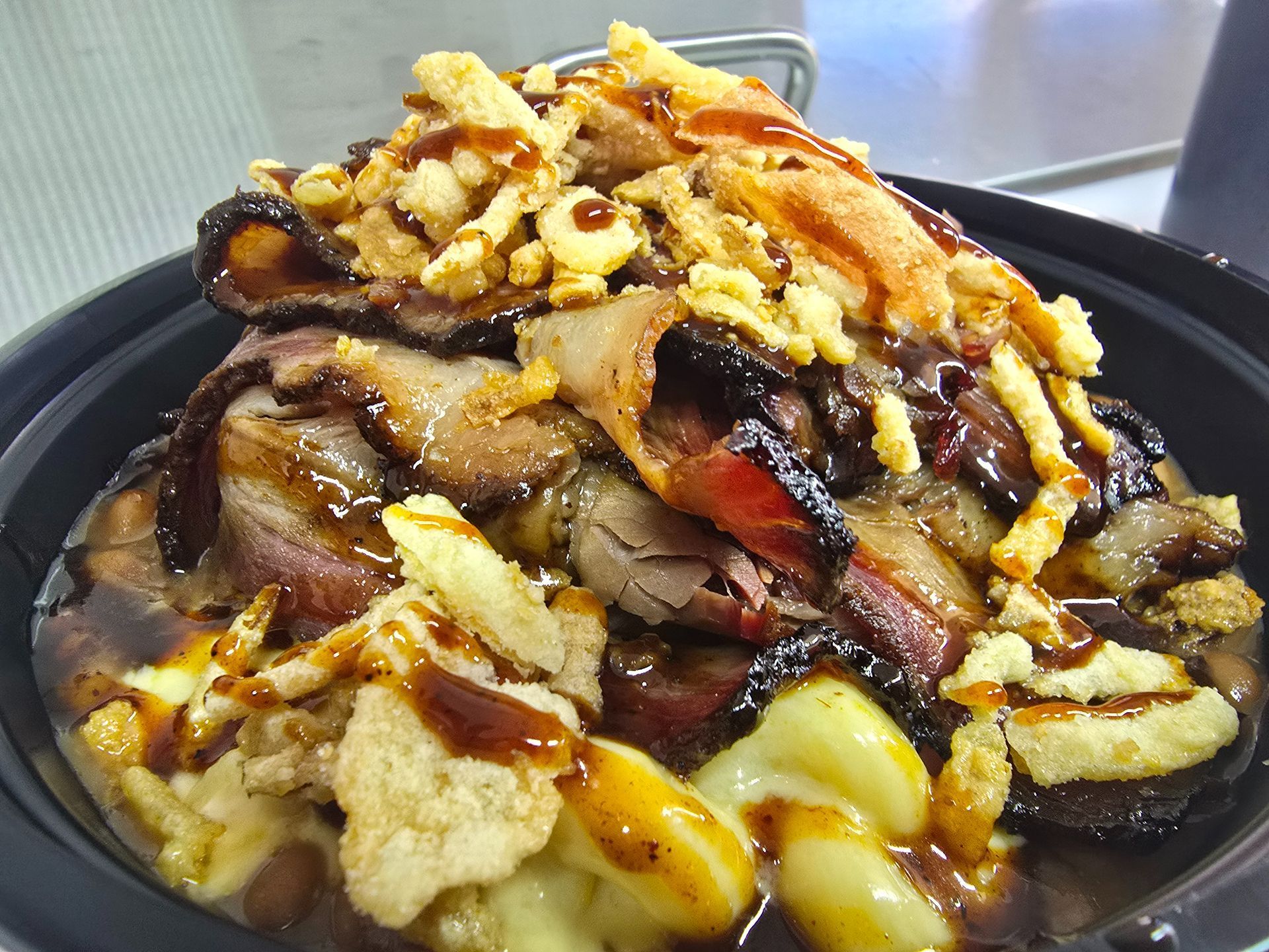 A bowl of rice topped with grilled meat, onions, and dark sauce on a table