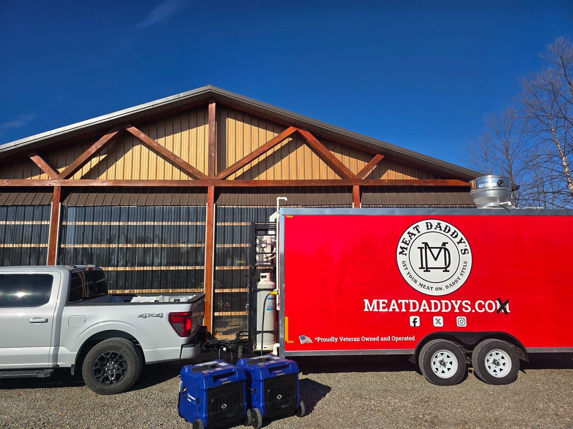 White pickup truck towing a red meat delivery trailer outside a wooden building