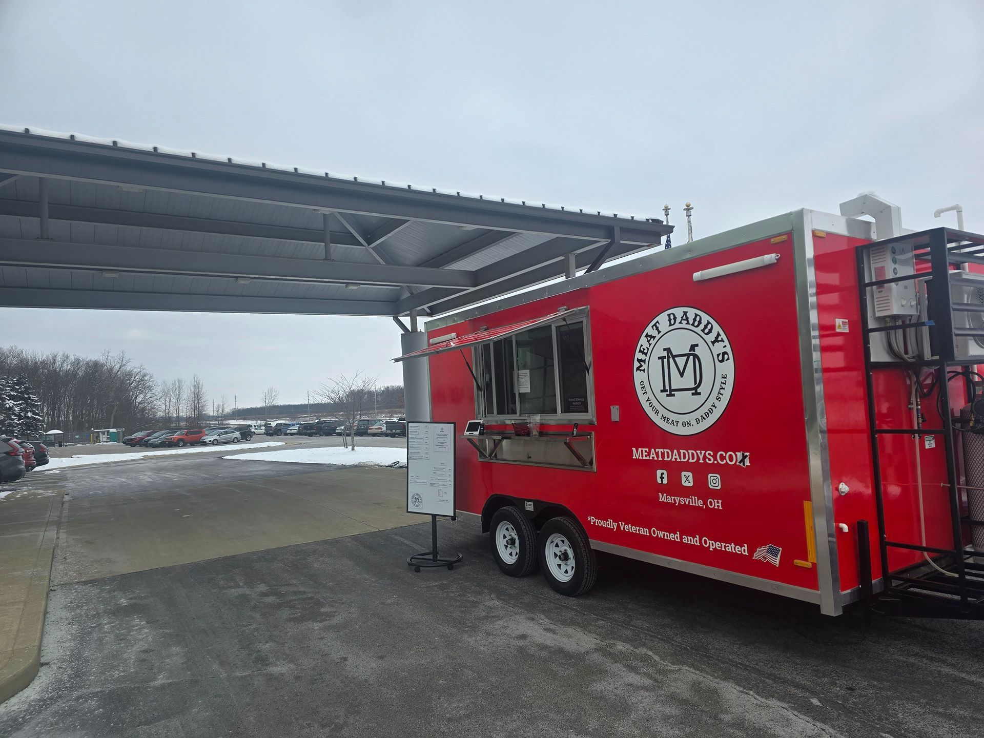 Red food truck parked under a covered shelter on a snowy day, with a service window open.